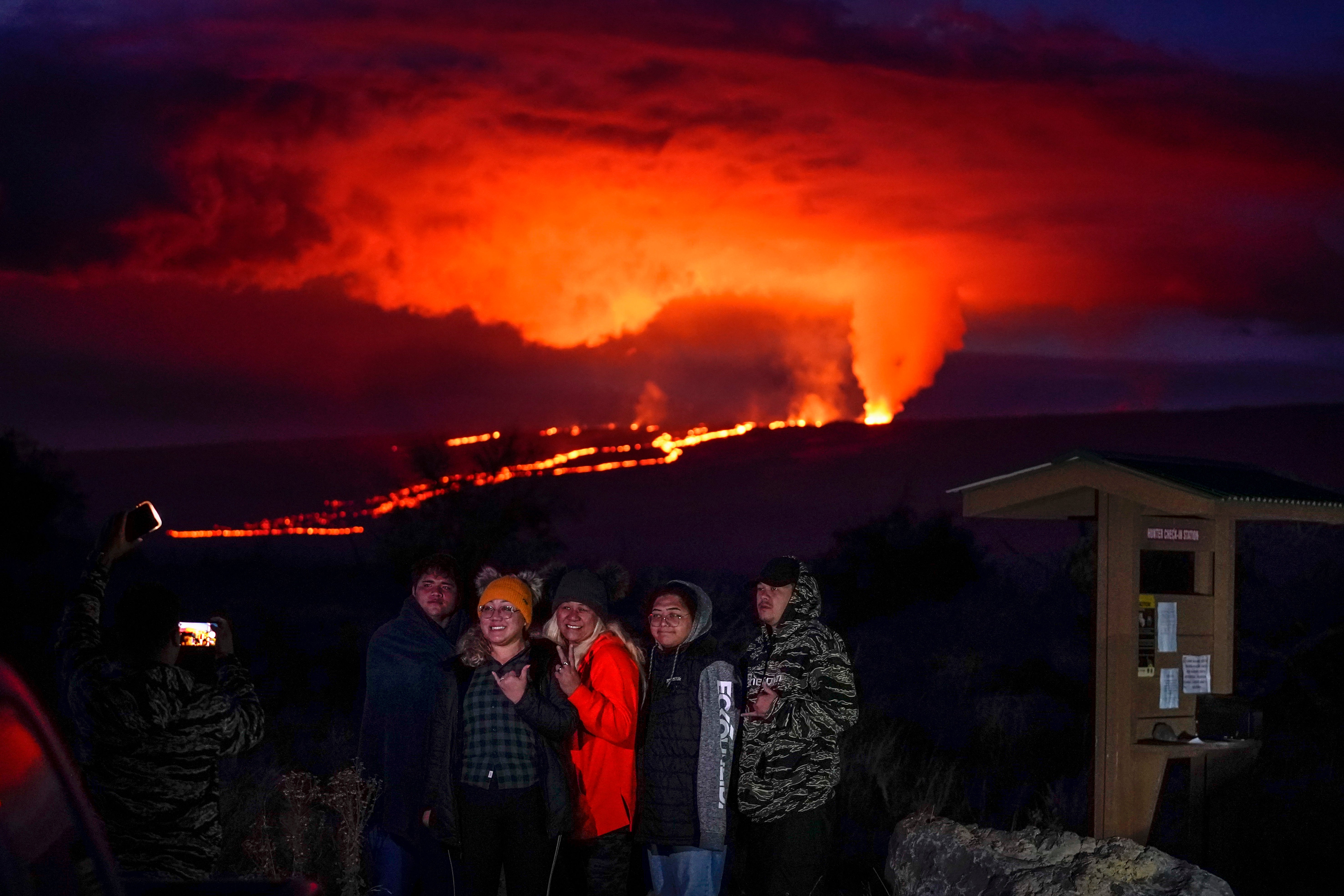 People pose for a photo in front of lava erupting from Hawaii's Mauna Loa volcano Wednesday, Nov. 30, 2022, near Hilo, Hawaii