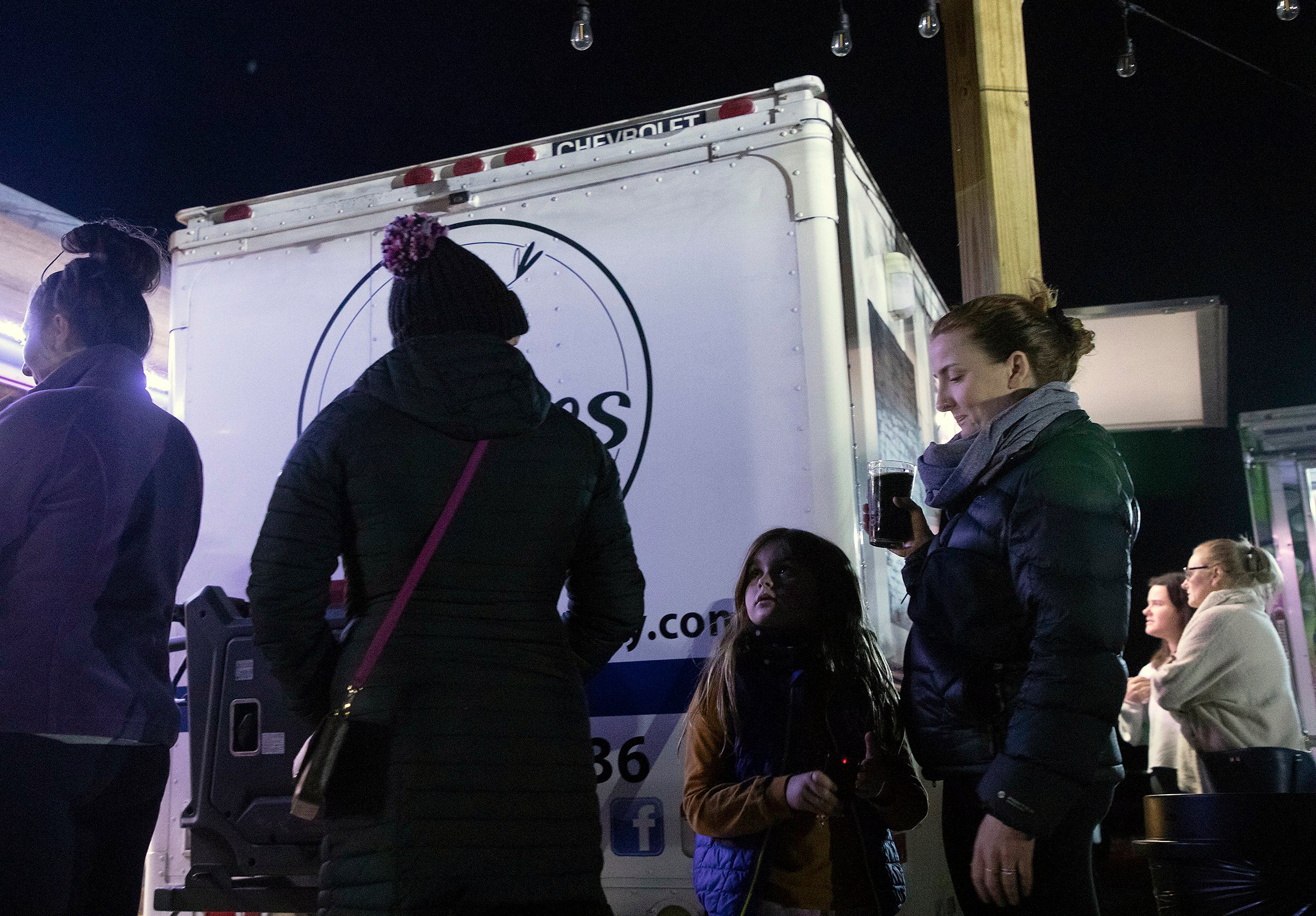 Elowyn Hoelscher, 7, stands in line at a food truck with her mother, Erika Hoelscher, at Red's Corner during the Moore County power outage on Monday in Southern Pines, N.C.