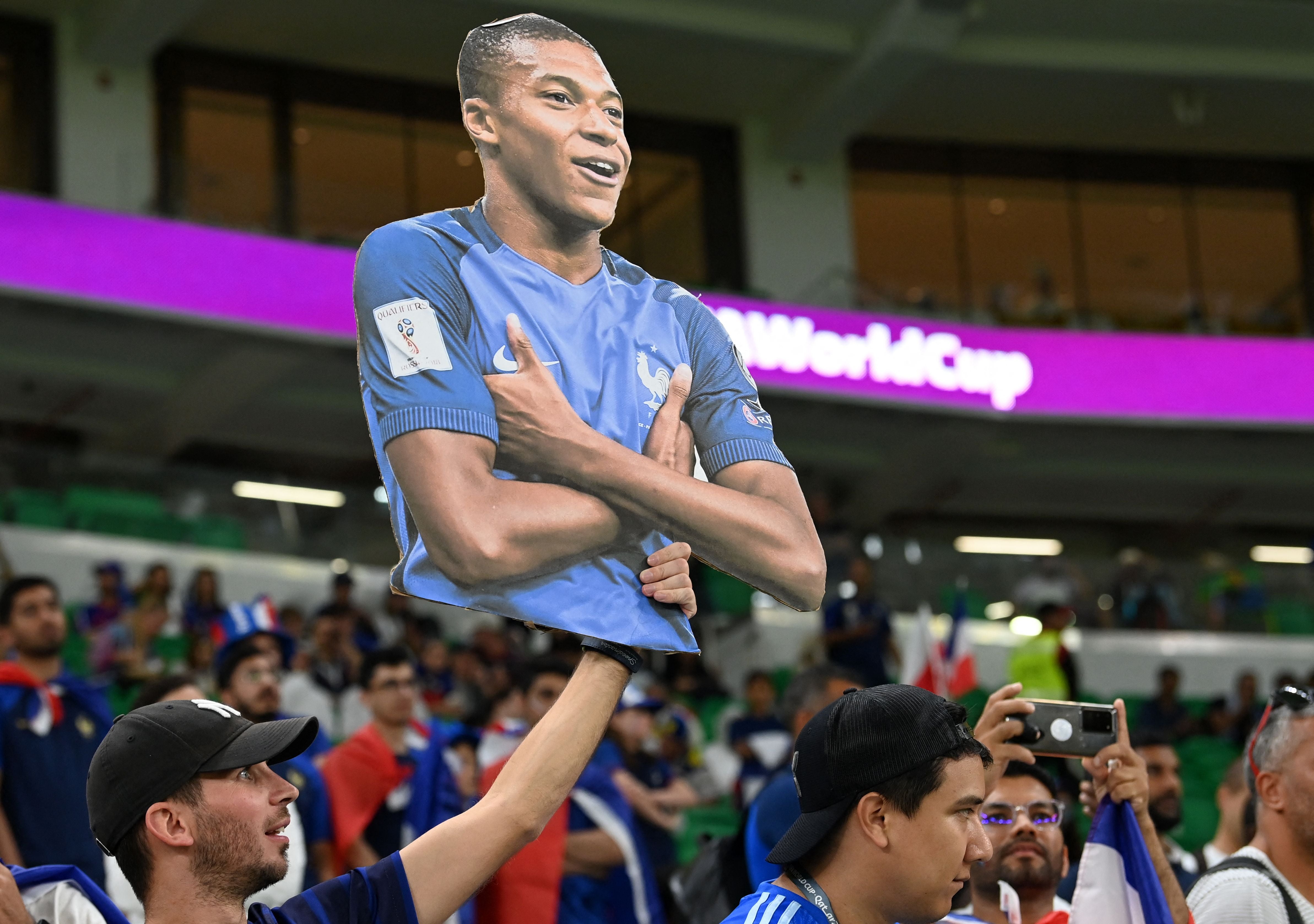 A France supporter carries a cardboard cutout of Kylian Mbappe