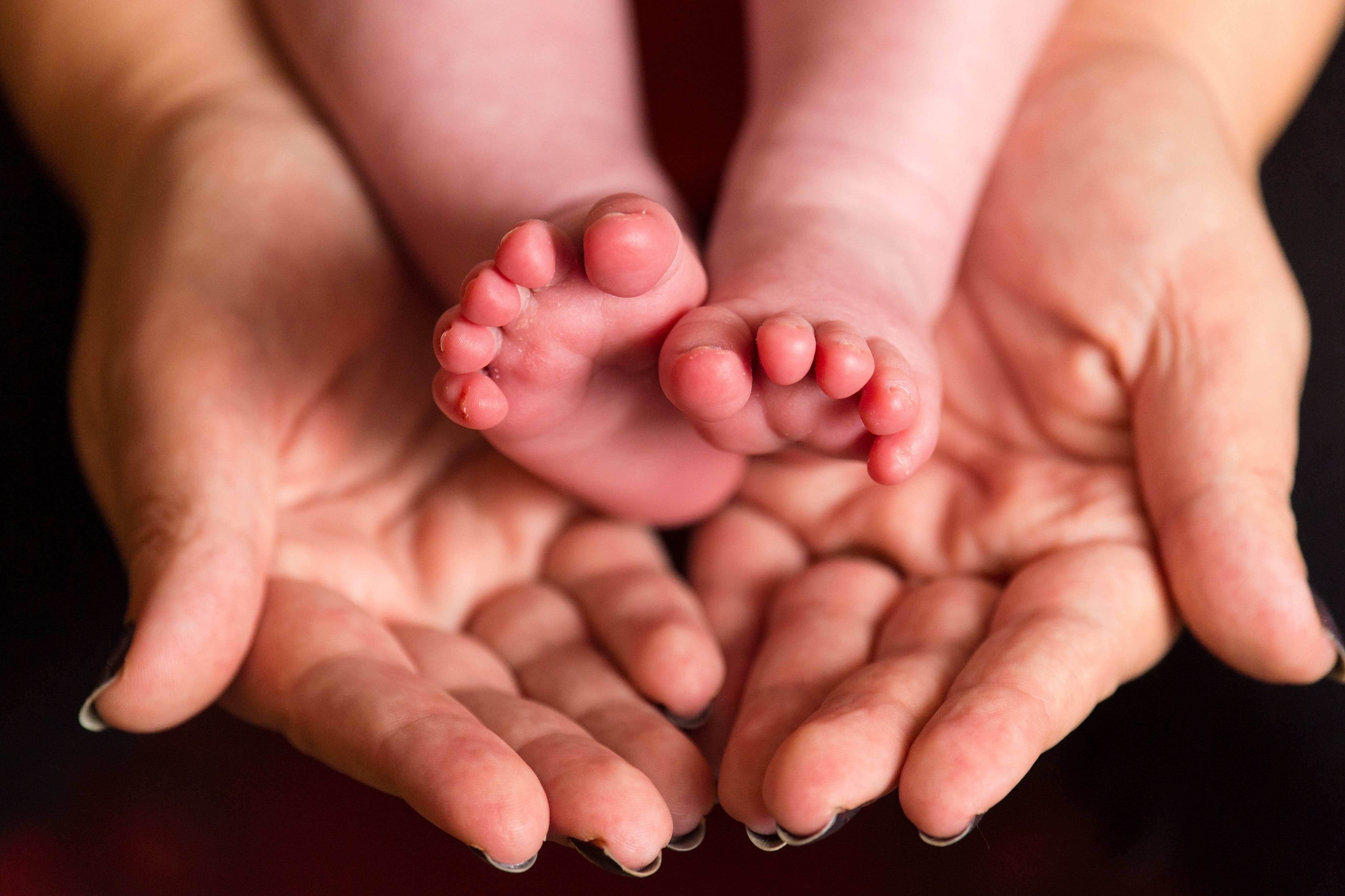 A mother holding the feet of a new baby (PA)