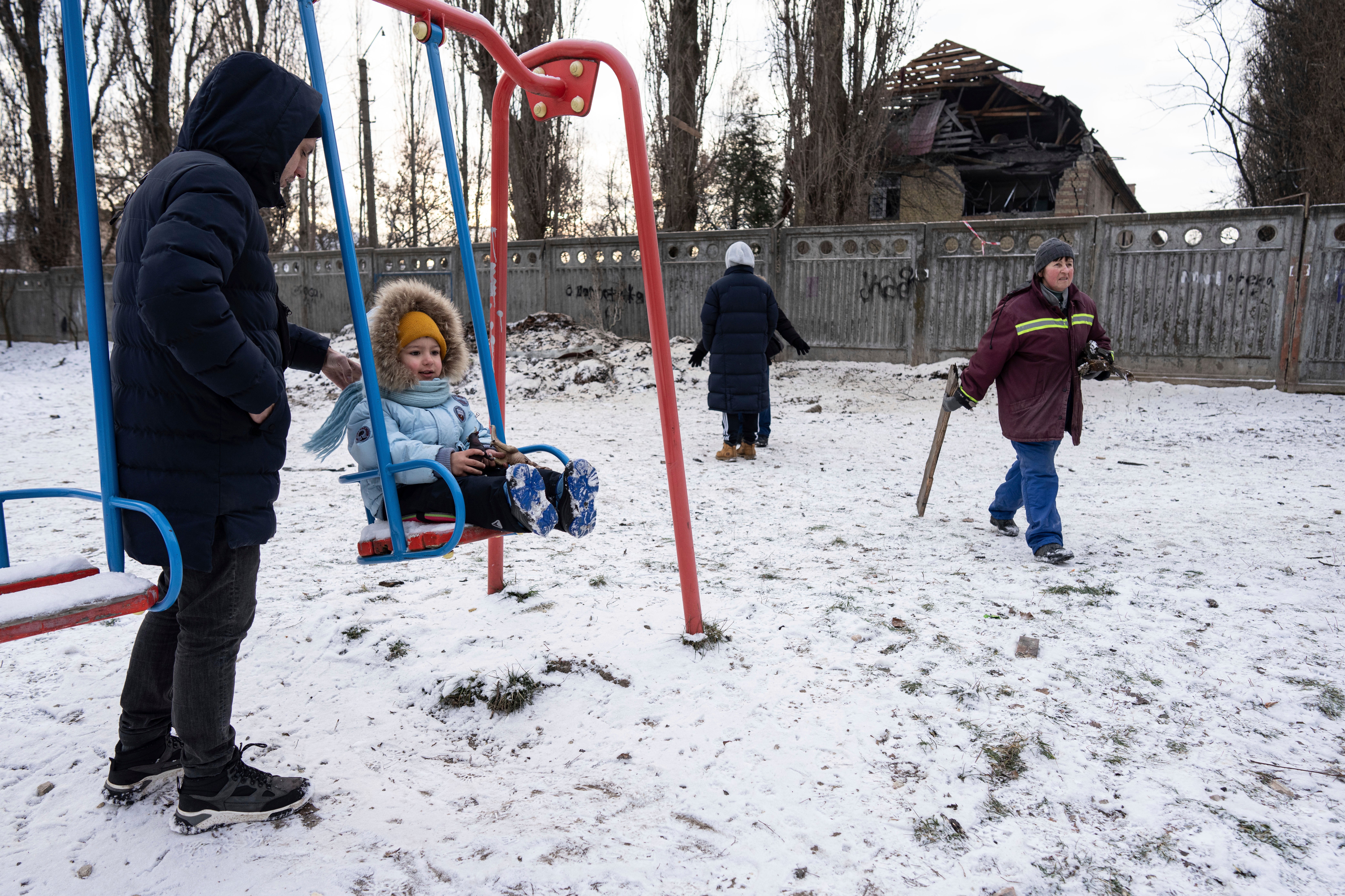 A man pushes his daughter on a swing in front of a tax office building that was heavily damaged by a Russian attack in Kyiv, Ukraine