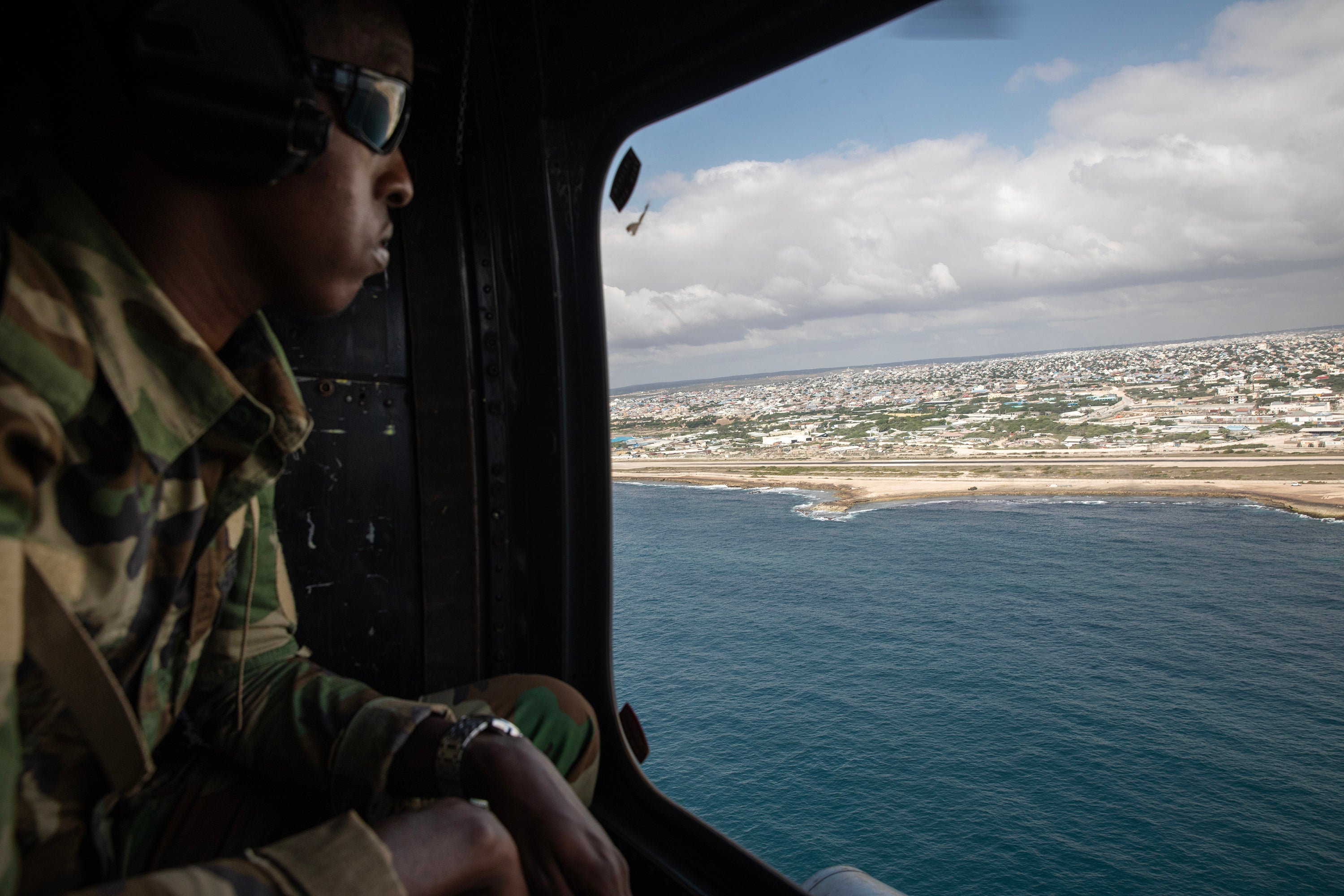 A soldier with the African Union Transition Mission looks at the landscape from a helicopter leaving Mogadishu