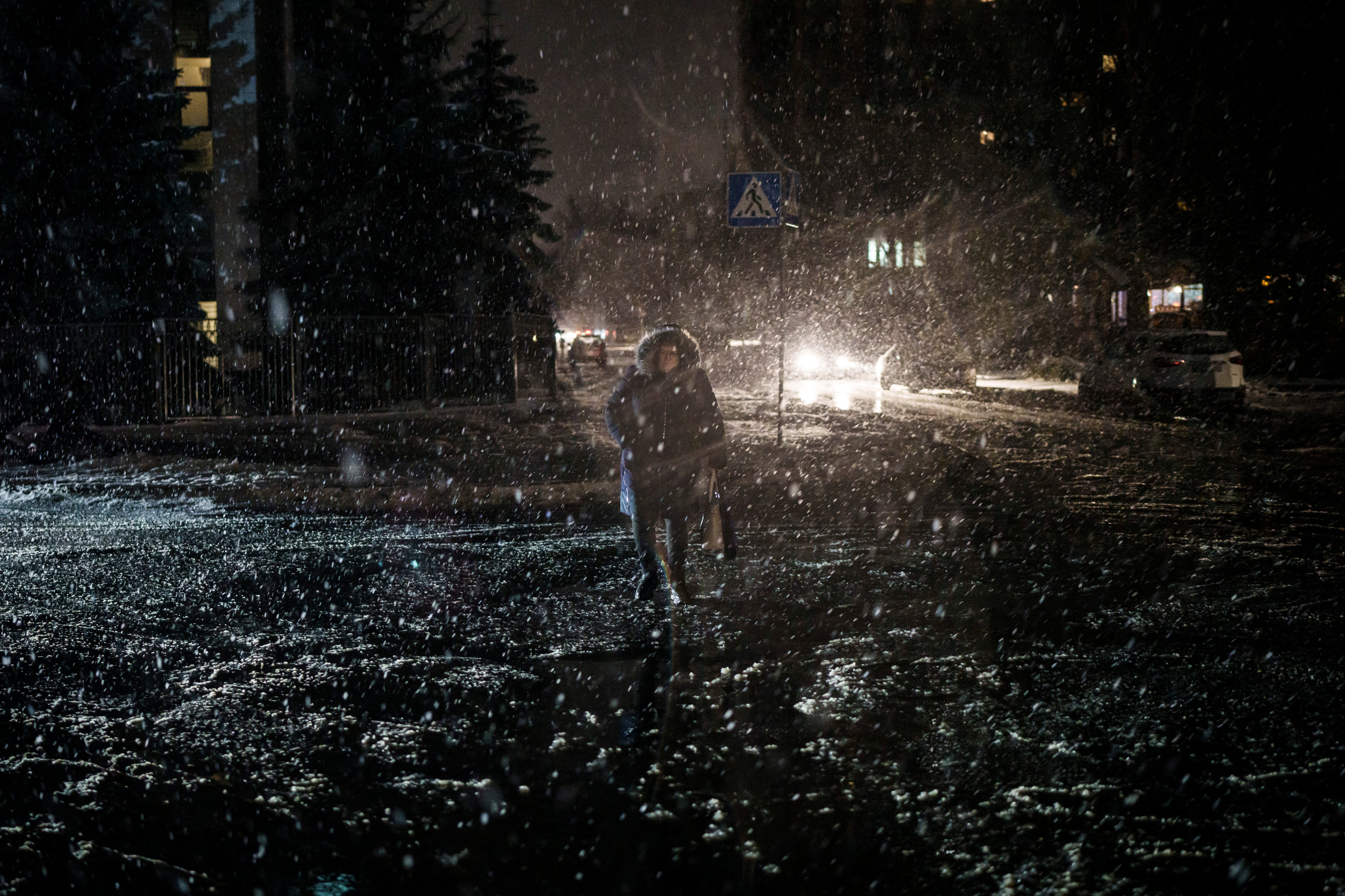 A woman crosses the street during snowfall, as power outages continue in Kyiv