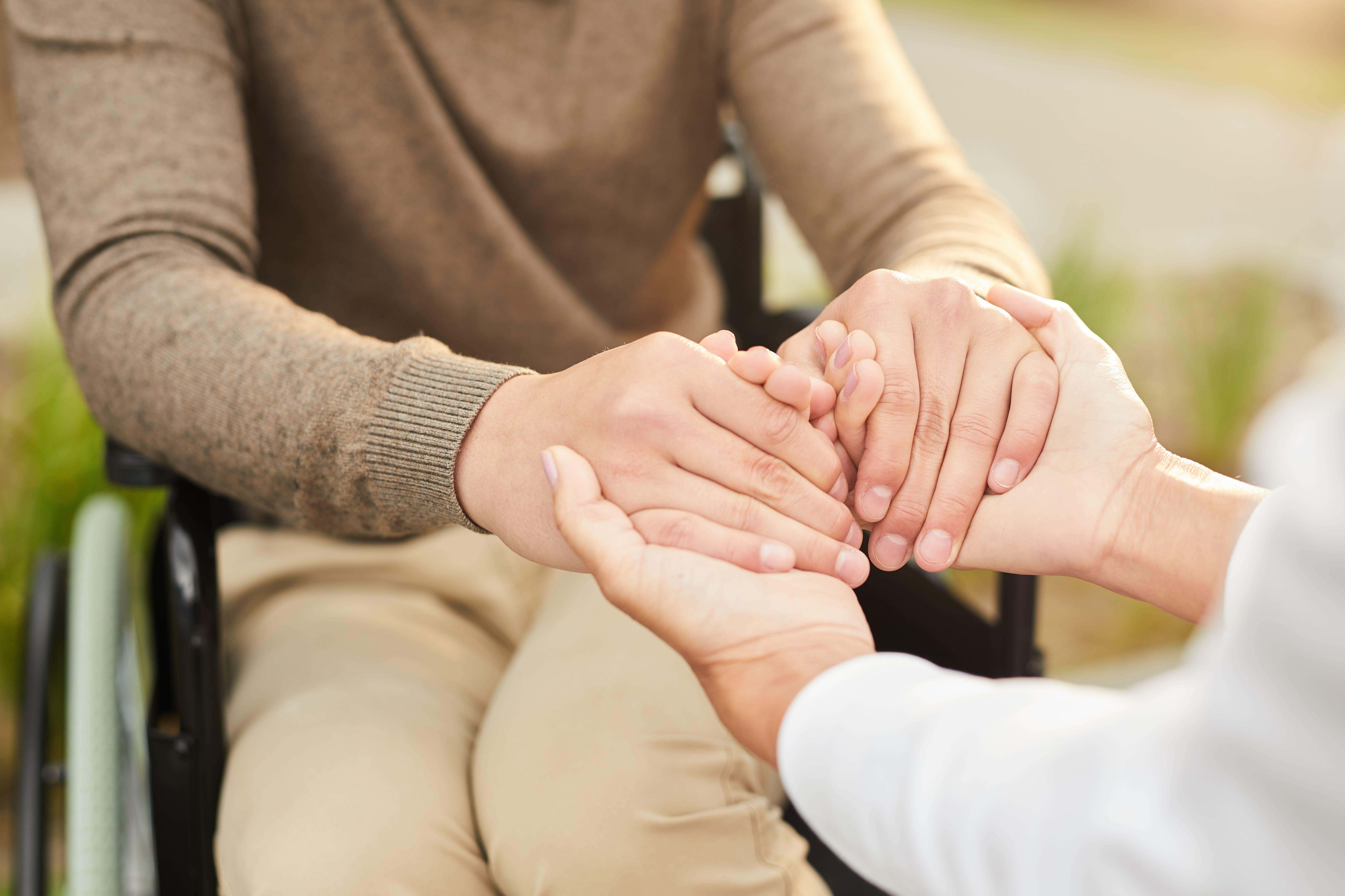 Close-up of unrecognizable social care worker and disabled patient in wheelchair holding hands (Contributor: Anastasia Pelikh / Alamy Stock Photo)