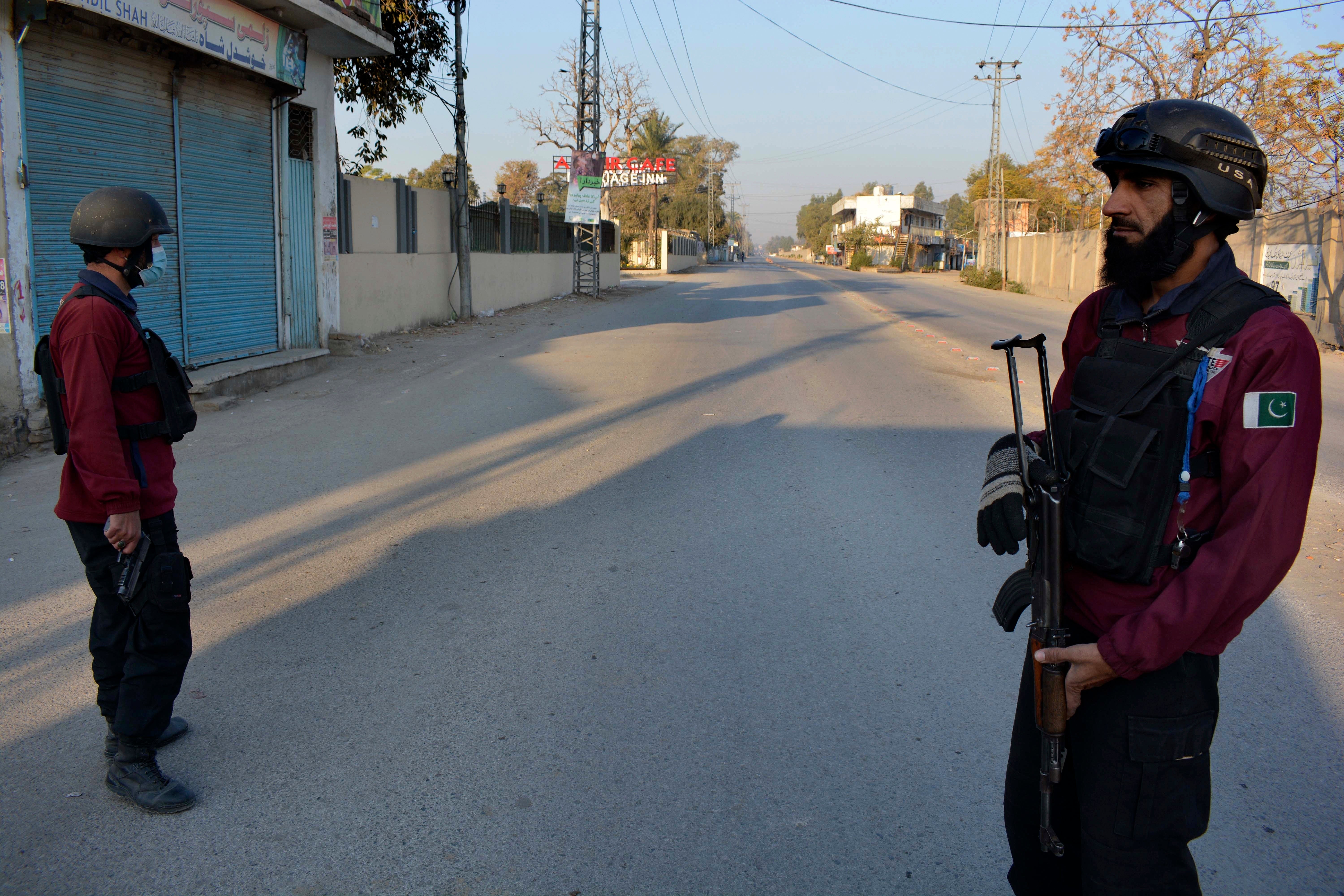 Security officials stand guard on a blocked road leading to a counter-terrorism center where several Pakistani Taliban detainees have taken police officers and others hostage inside the compound