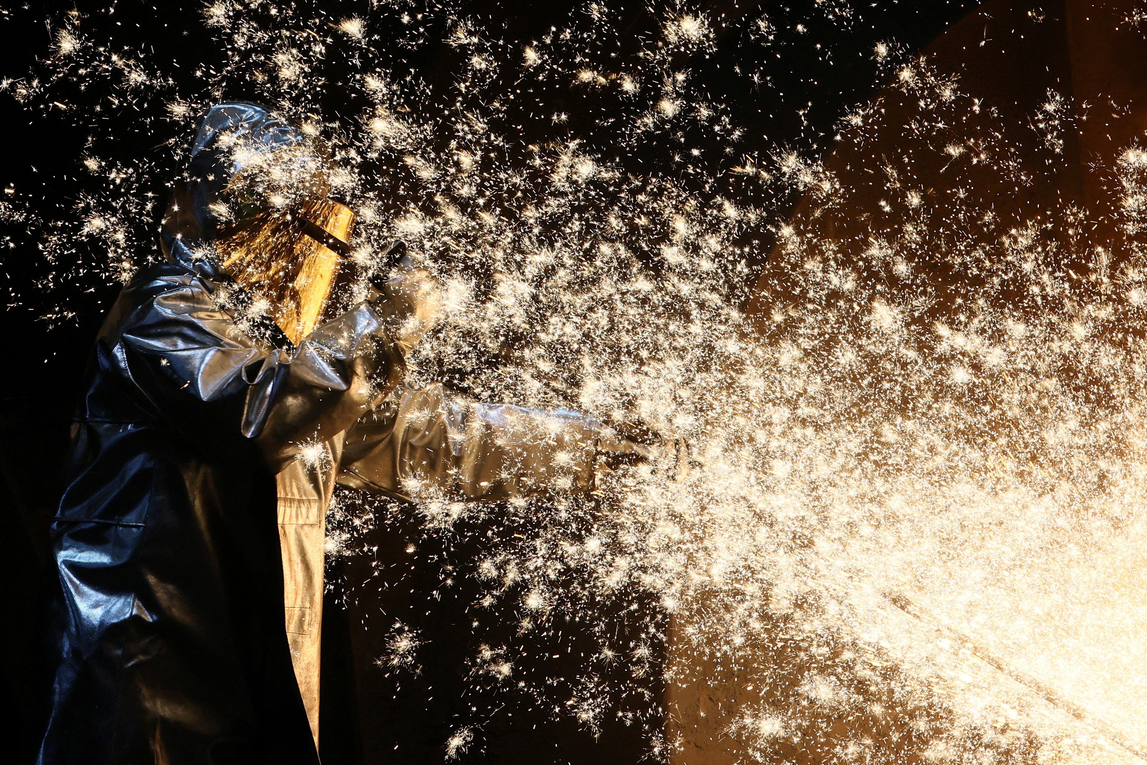 A steel worker of ThyssenKrupp stands amid sparks of raw iron coming from a blast furnace at a ThyssenKrupp steel factory in Duisburg, western Germany