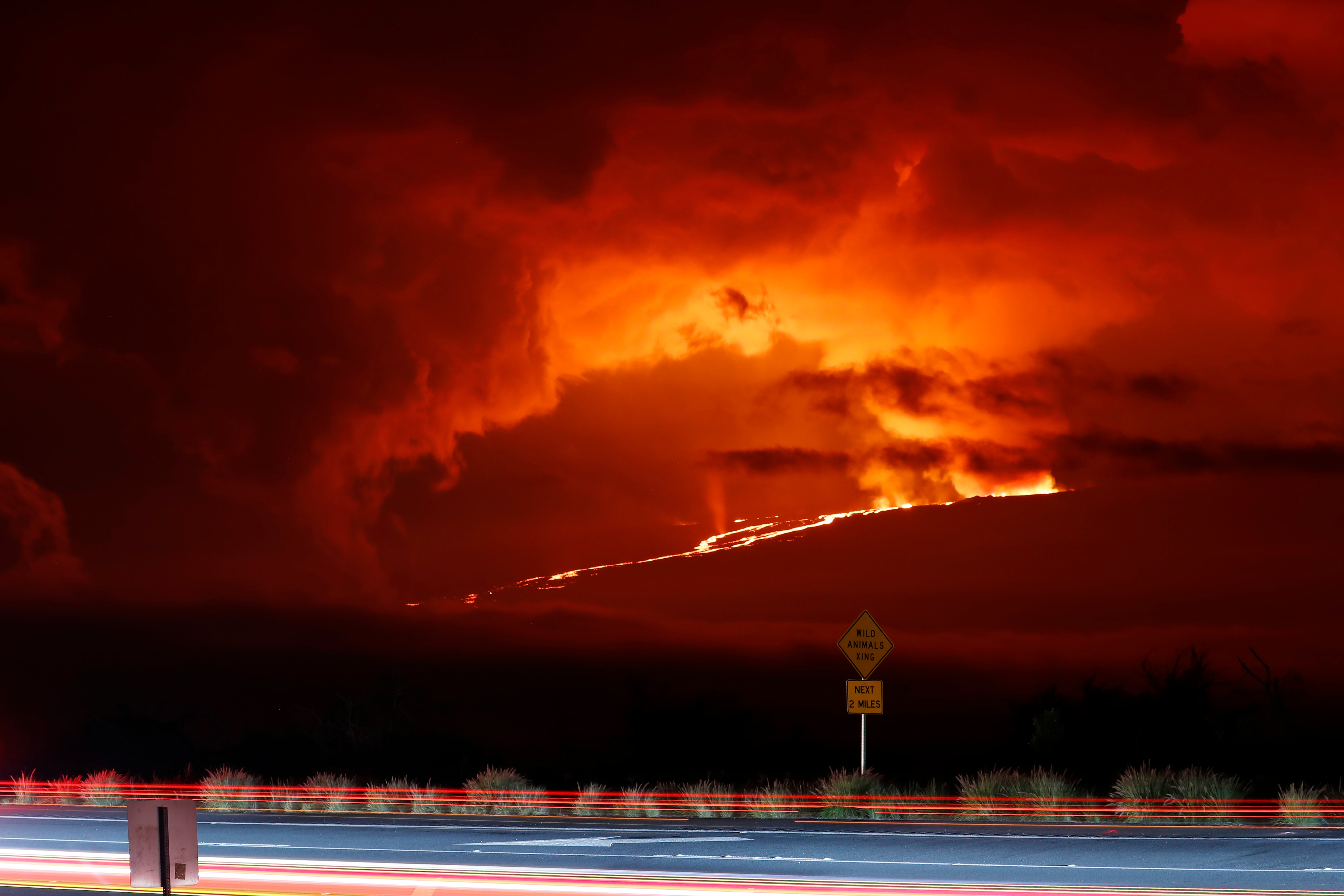 In this long camera exposure, cars drive down Saddle Road as Mauna Loa erupts in the distance near Hilo, Hawaii