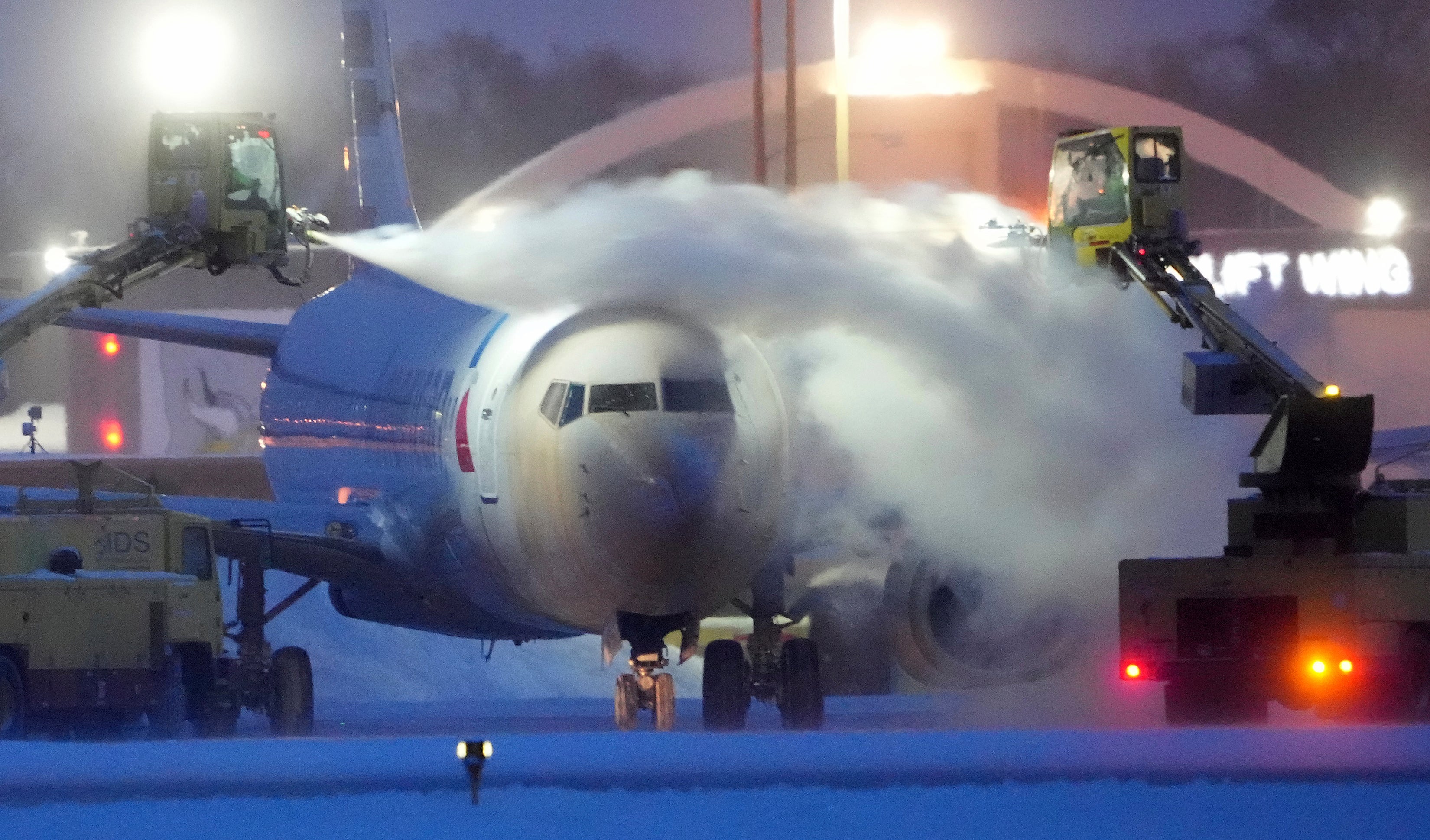 An American Airlines plane is de-iced as high winds whip around 7.5 inches of new snow at Minneapolis-St. Paul International Airport Thursday, Dec. 22, 2022