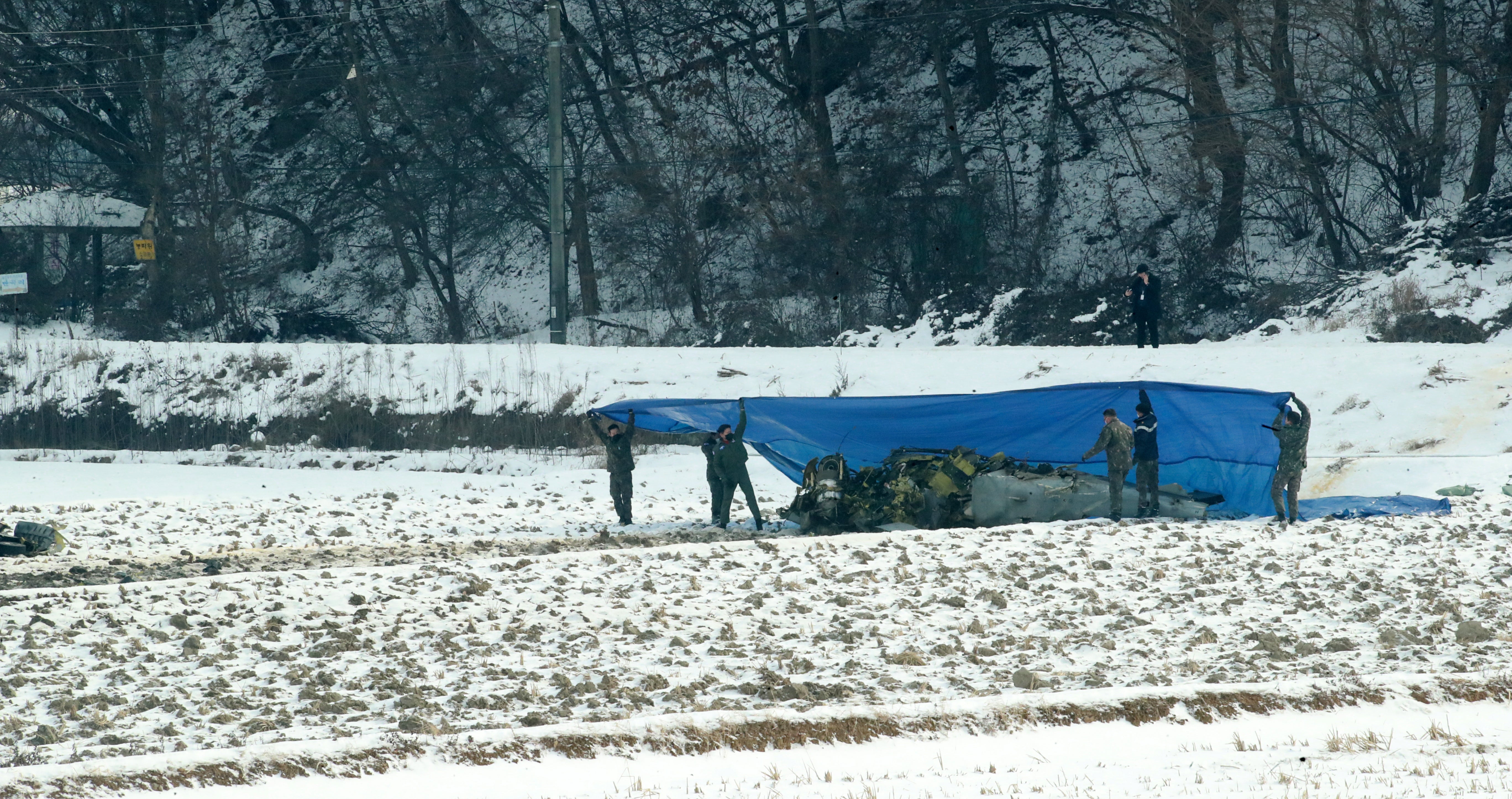 Military police cover the wreckage of a South Korean KA-1 light attack aircraft with a blue plastic sheet after it crashed on a rice paddy in Hoengseong, Gangwon province on 26 December