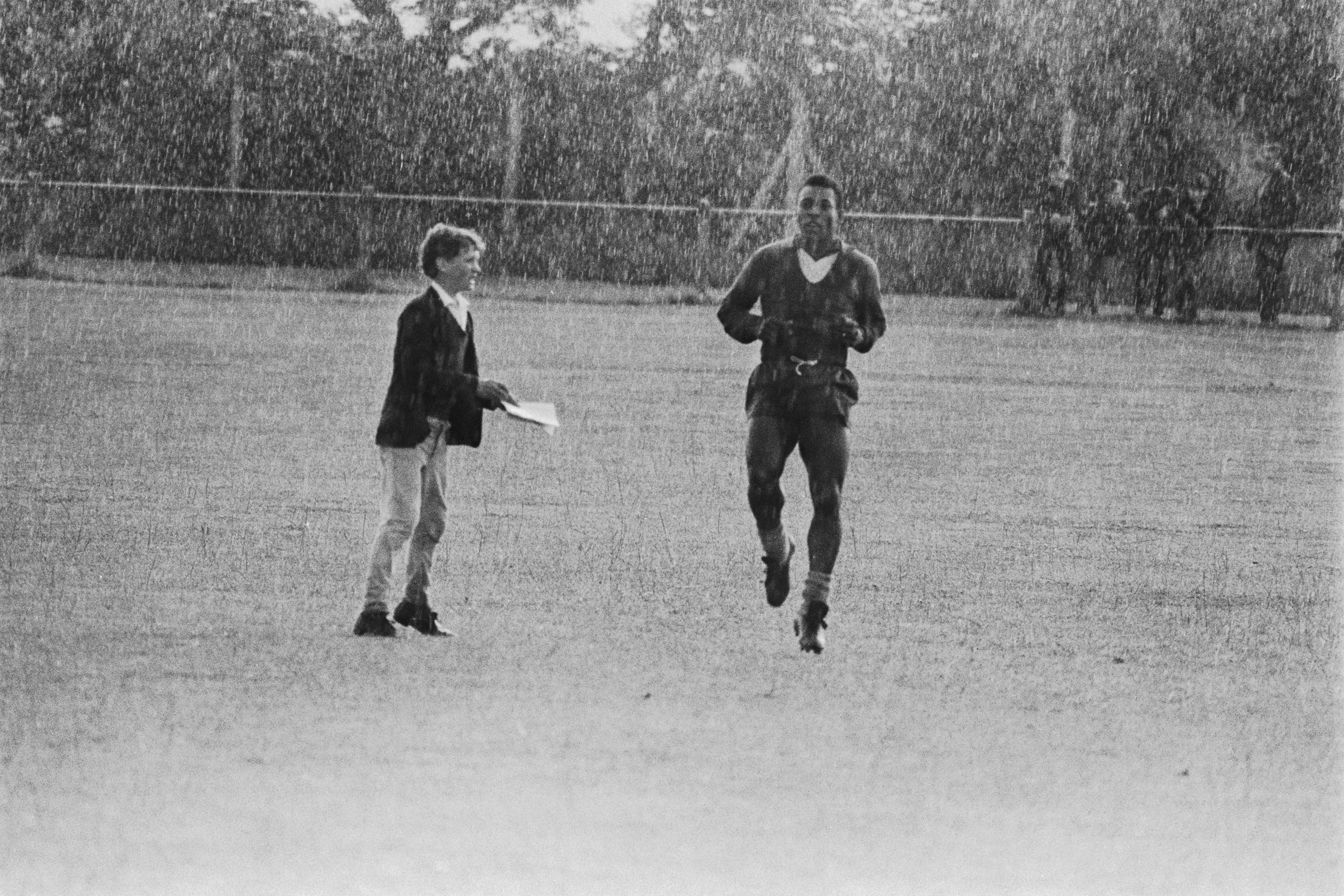 A young fan approaches Pele for an autograph while he is training in the pouring rain in Bolton in preparation for Brazils match against Portugal, 18th July 1966.