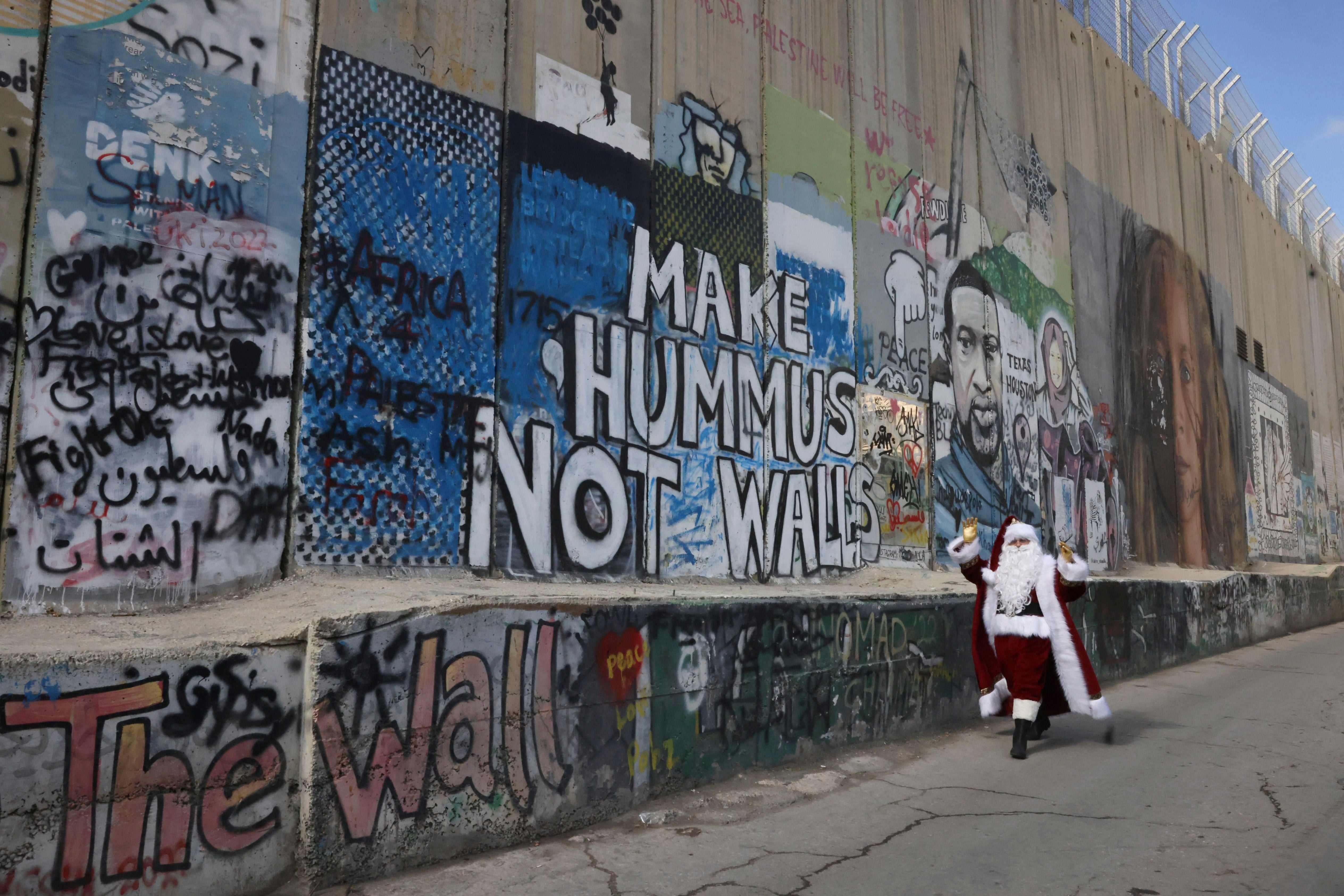 A man dressed in a Santa outfit walks alongside Israel’s separation wall in the biblical West Bank city of Bethlehem on 22 December