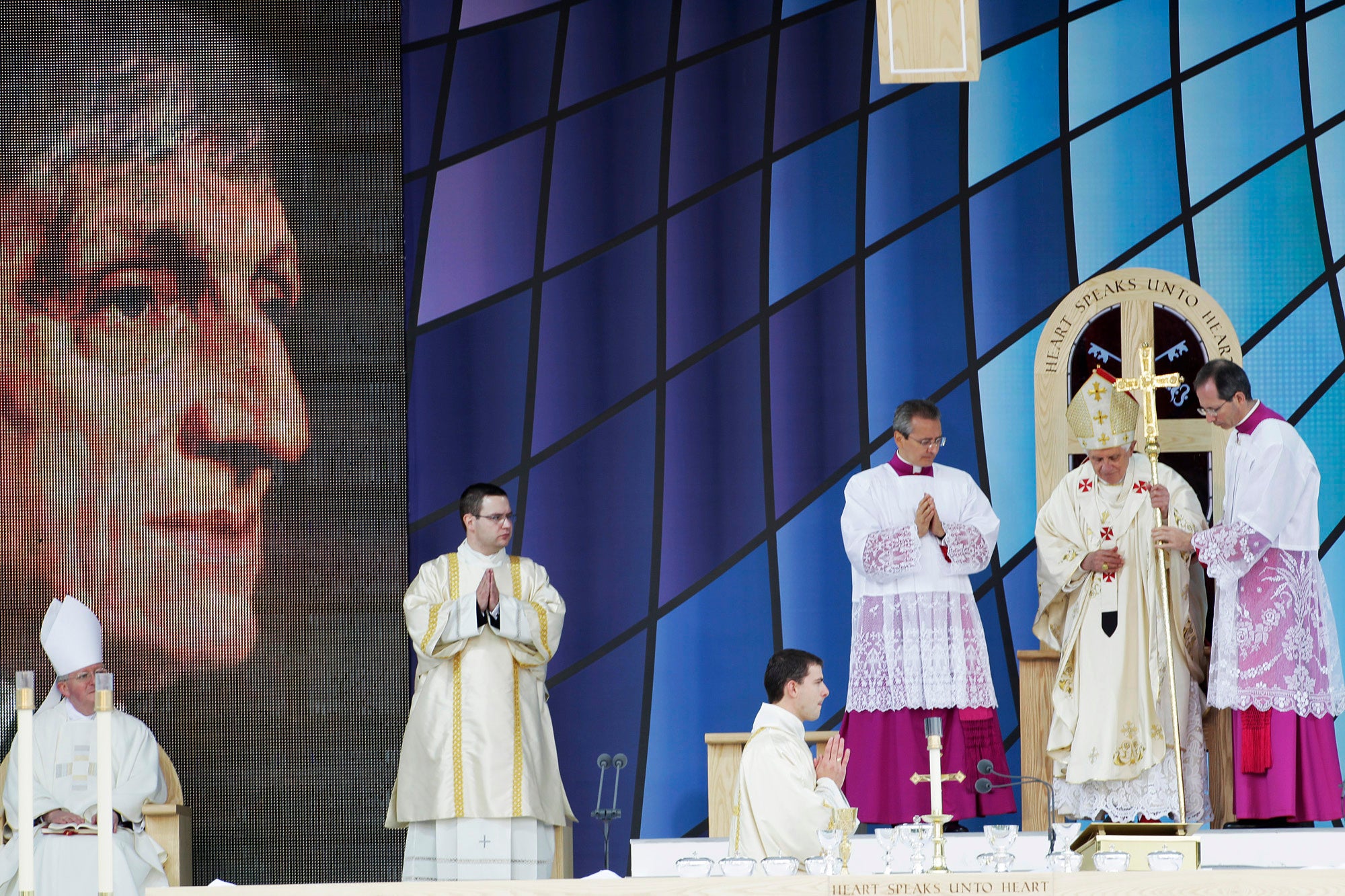 Pope Benedict XVI walks with a cross as he celebrates a beatification mass for Cardinal John Henry Newman, pictured on a giant screen at left, in Birmingham, England, on 19 September 2010