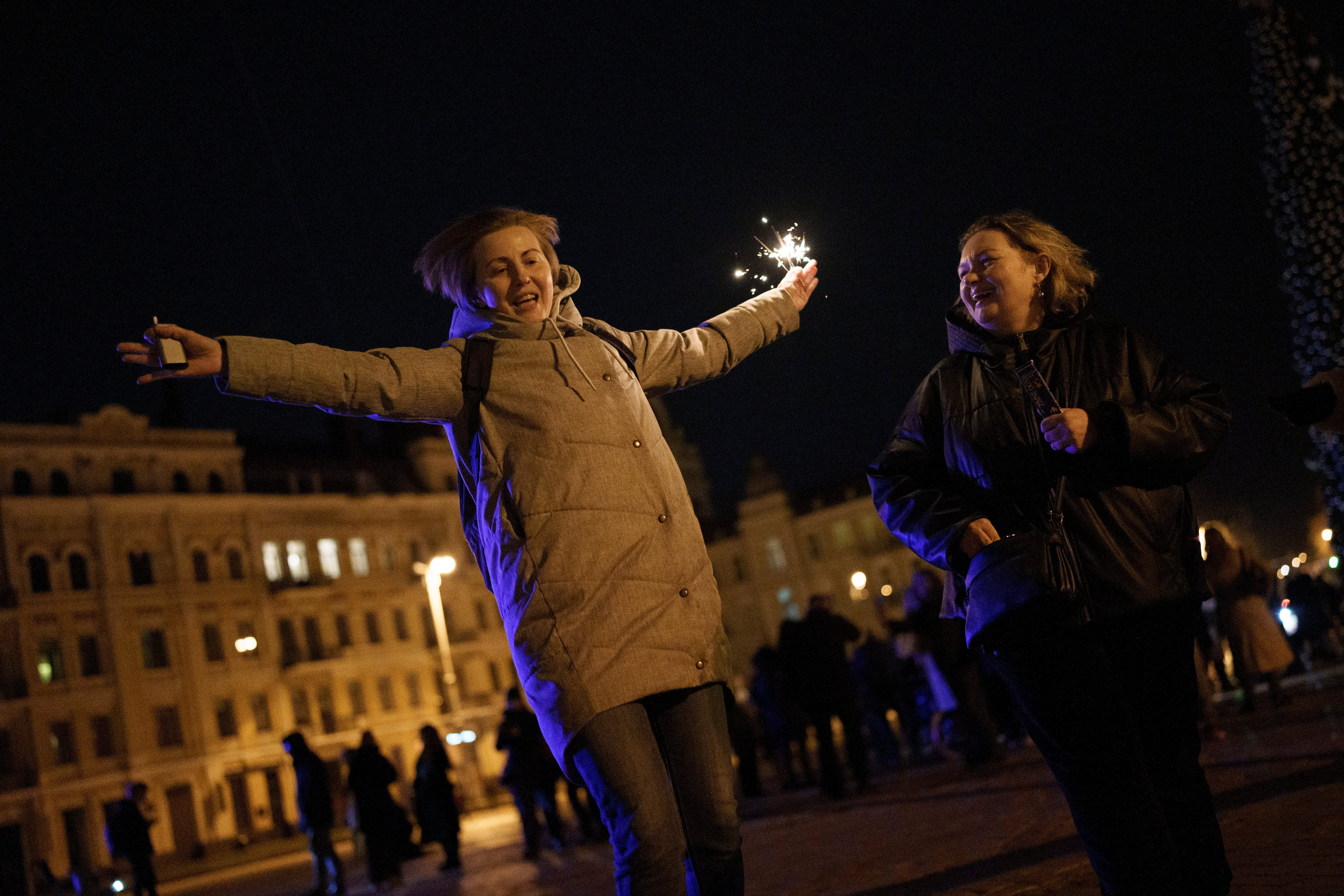 A woman holds a sparkler as she dances in Sophia Square before curfew on New Year's Eve in Kyiv