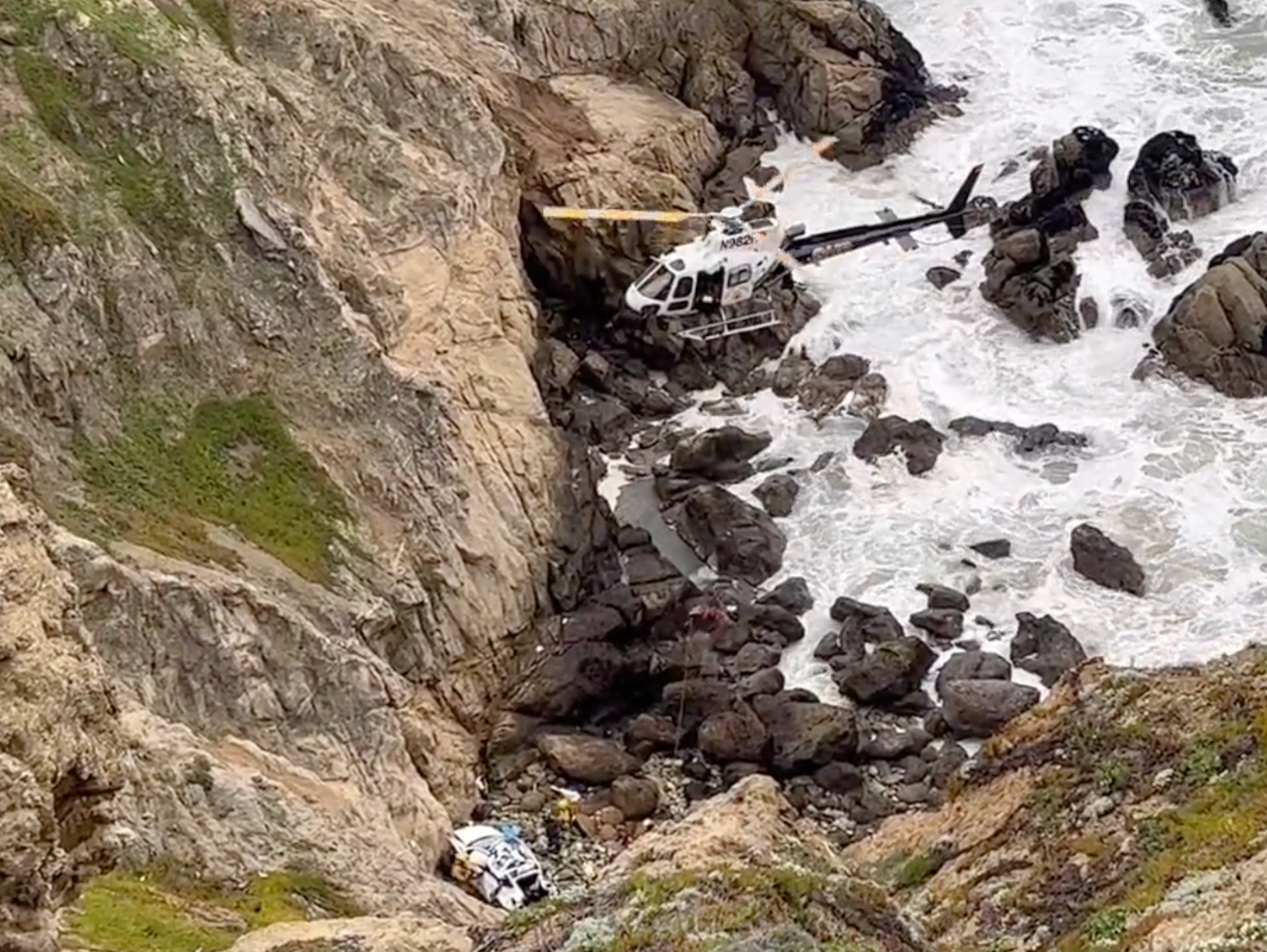 A helicopter hovers over the crashed vehicle as rescuers try to get to the injured driver and passengers