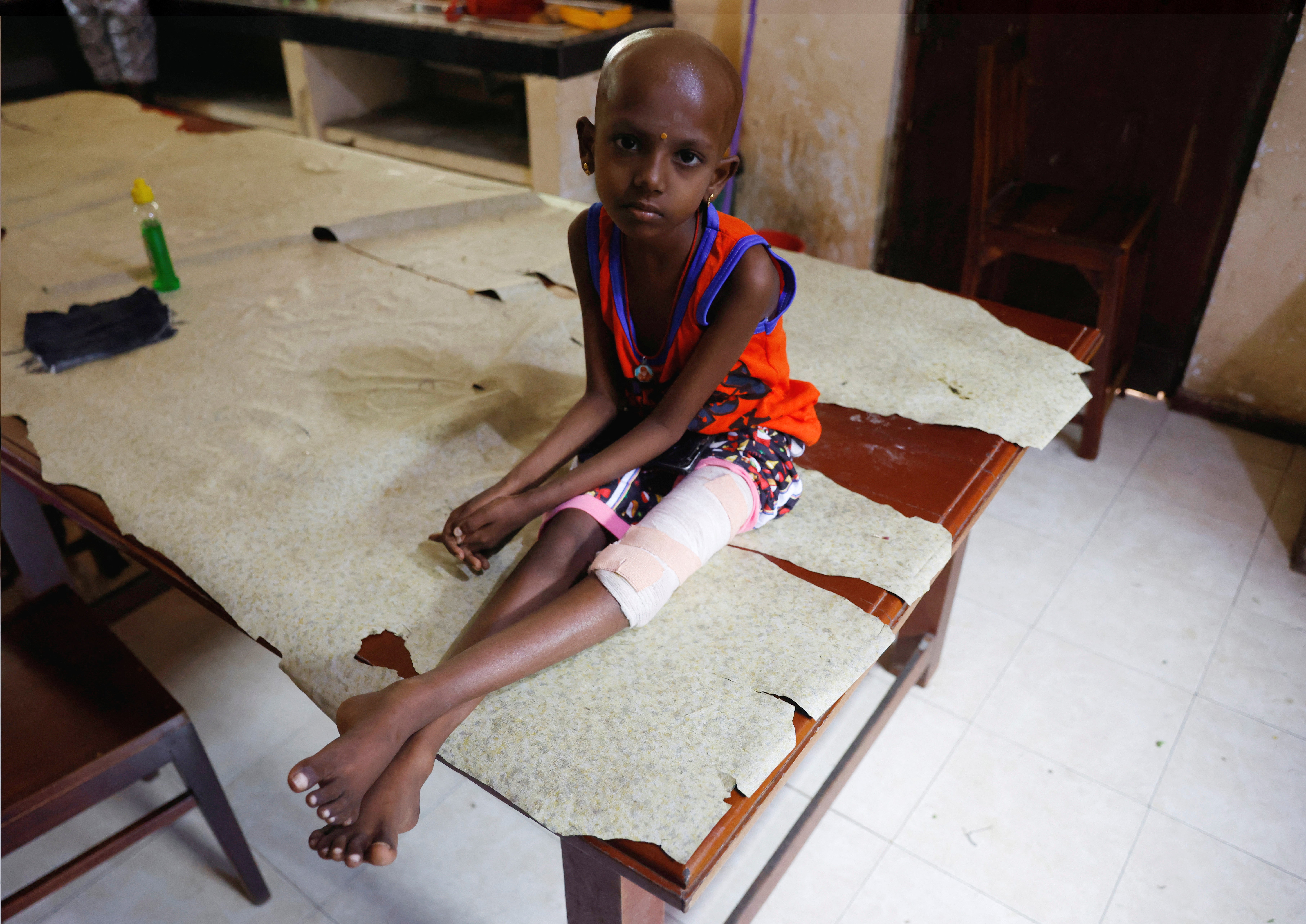 Rathis Supiksa, 7, who has both blood cancer and bone cancer in her leg, sits on a table in a communal kitchen while her aunt cooks food