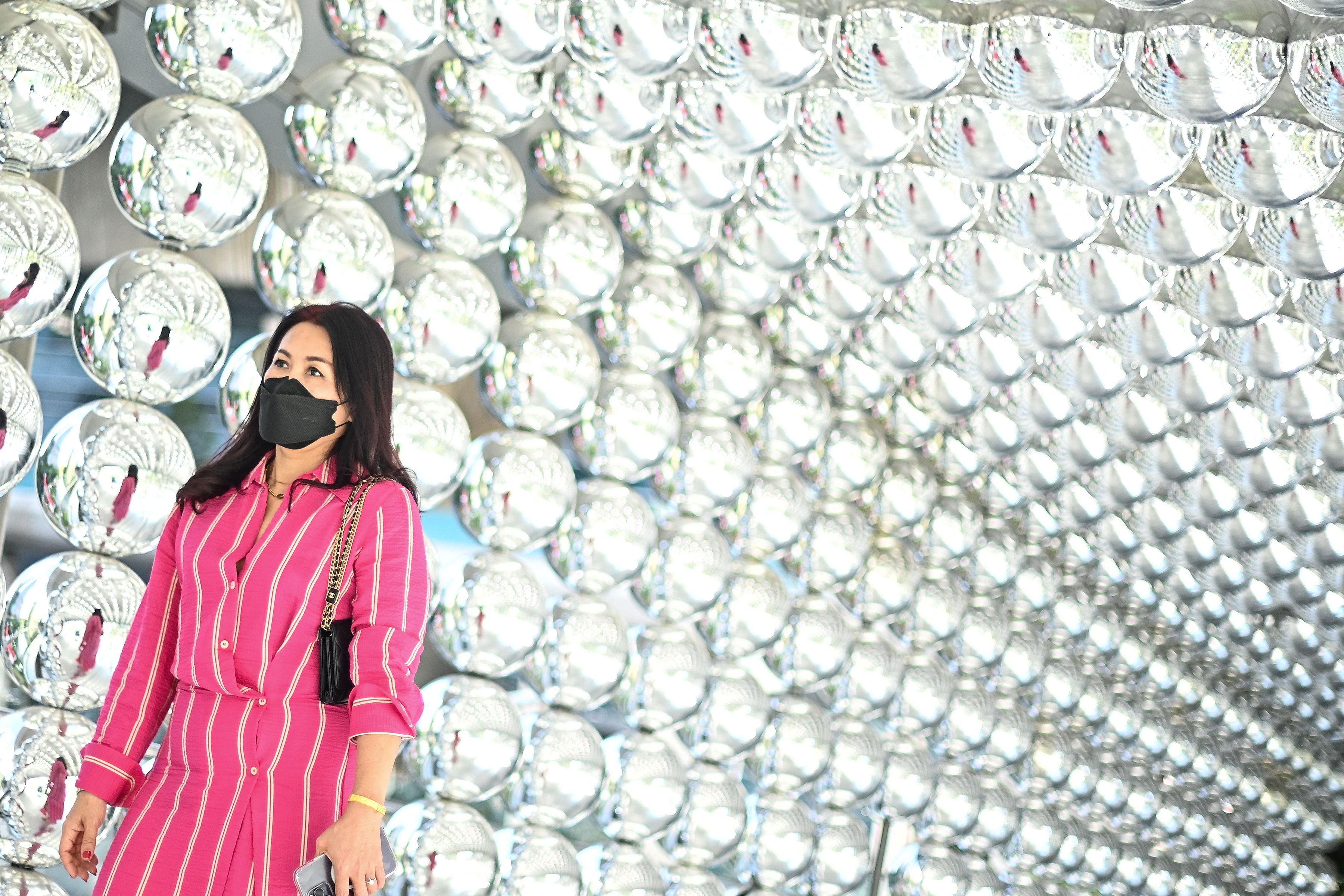 A woman walks past a decoration made of reflective balls outside a shopping mall in Bangkok