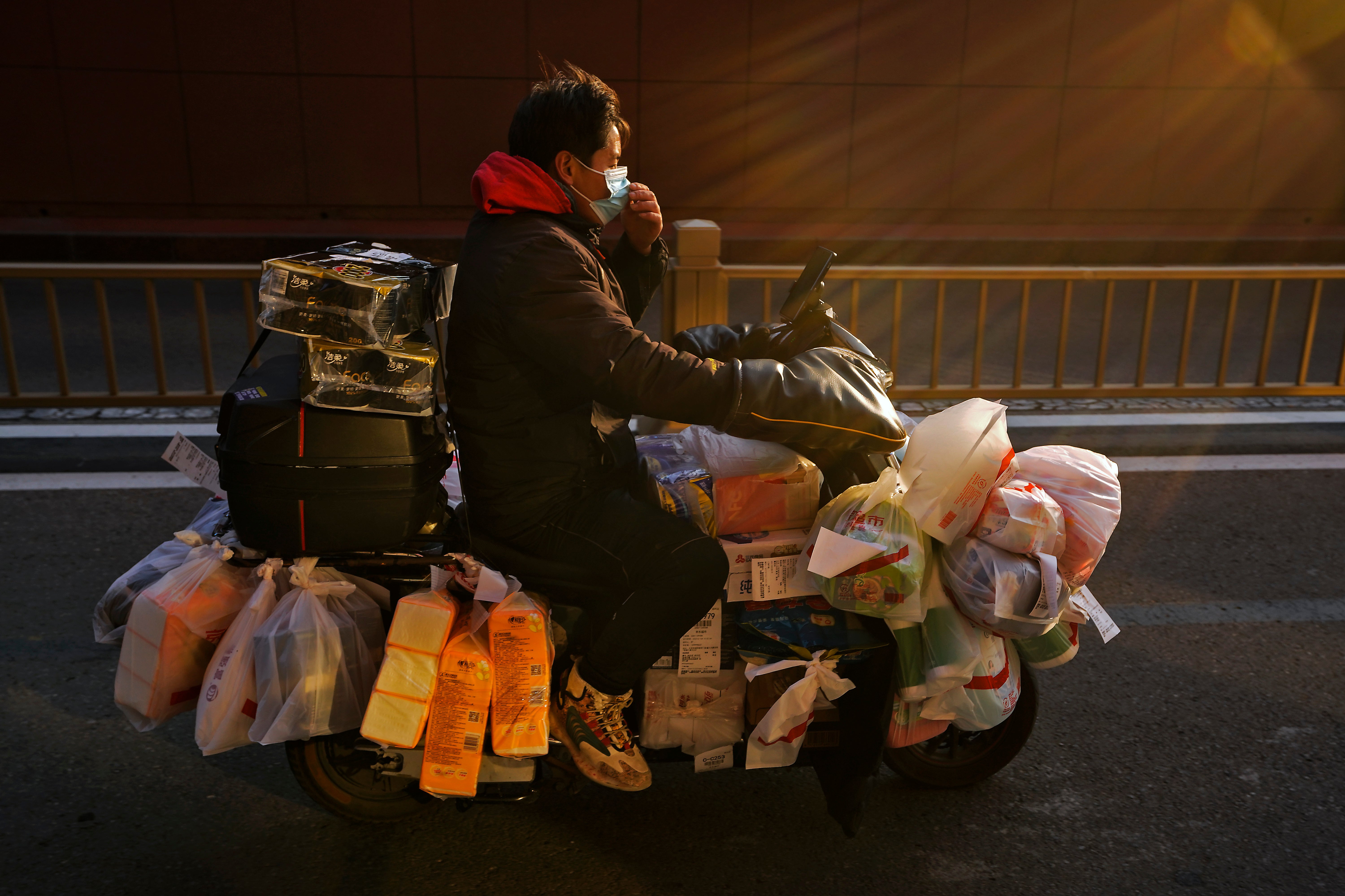 A delivery worker adjusts his face mask as he rides on his bike loaded with customers' online order groceries on a street in Beijing