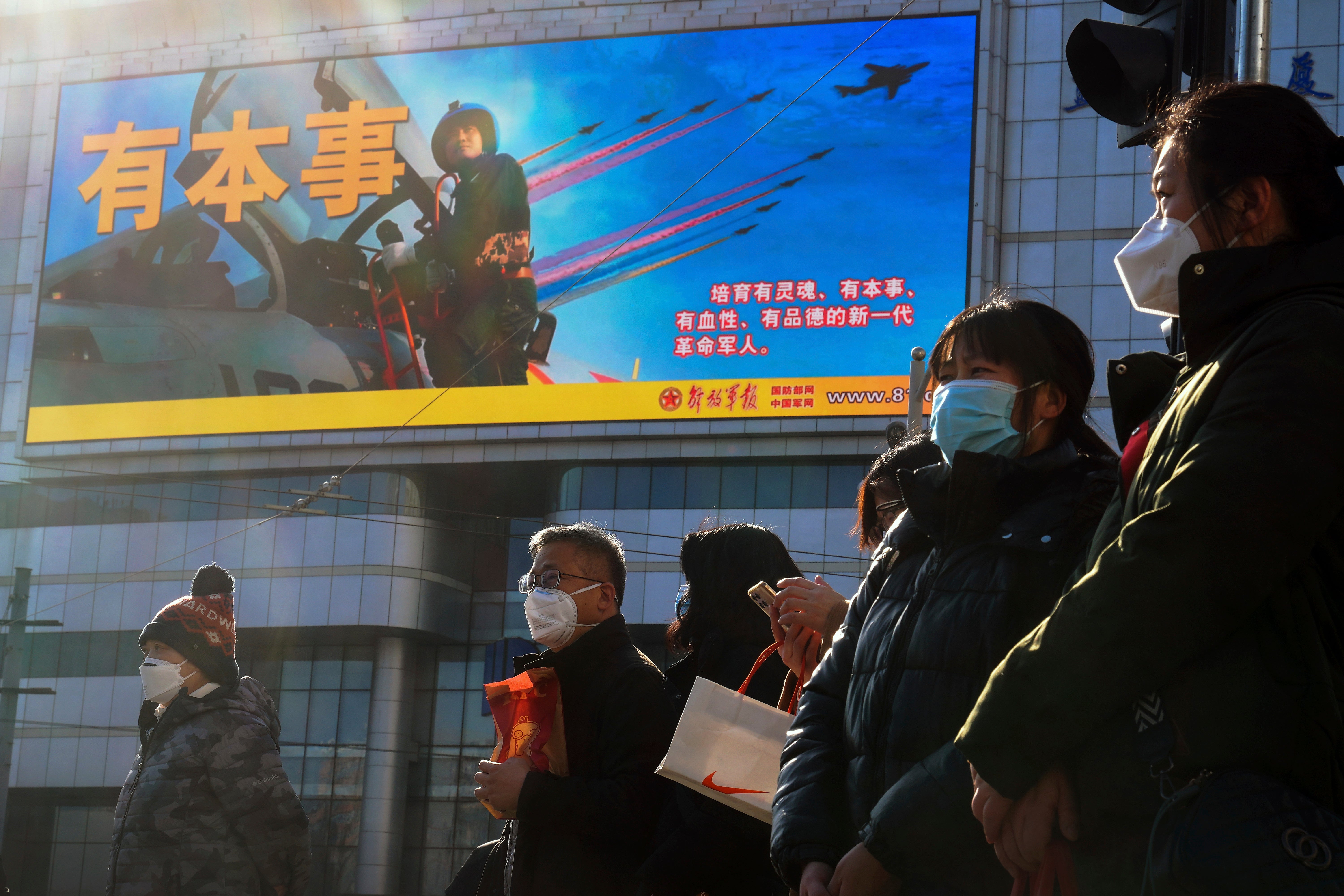 Residents wearing face masks wait to cross a traffic intersection near a large screen promoting the Chinese People's Liberation Army Airforce