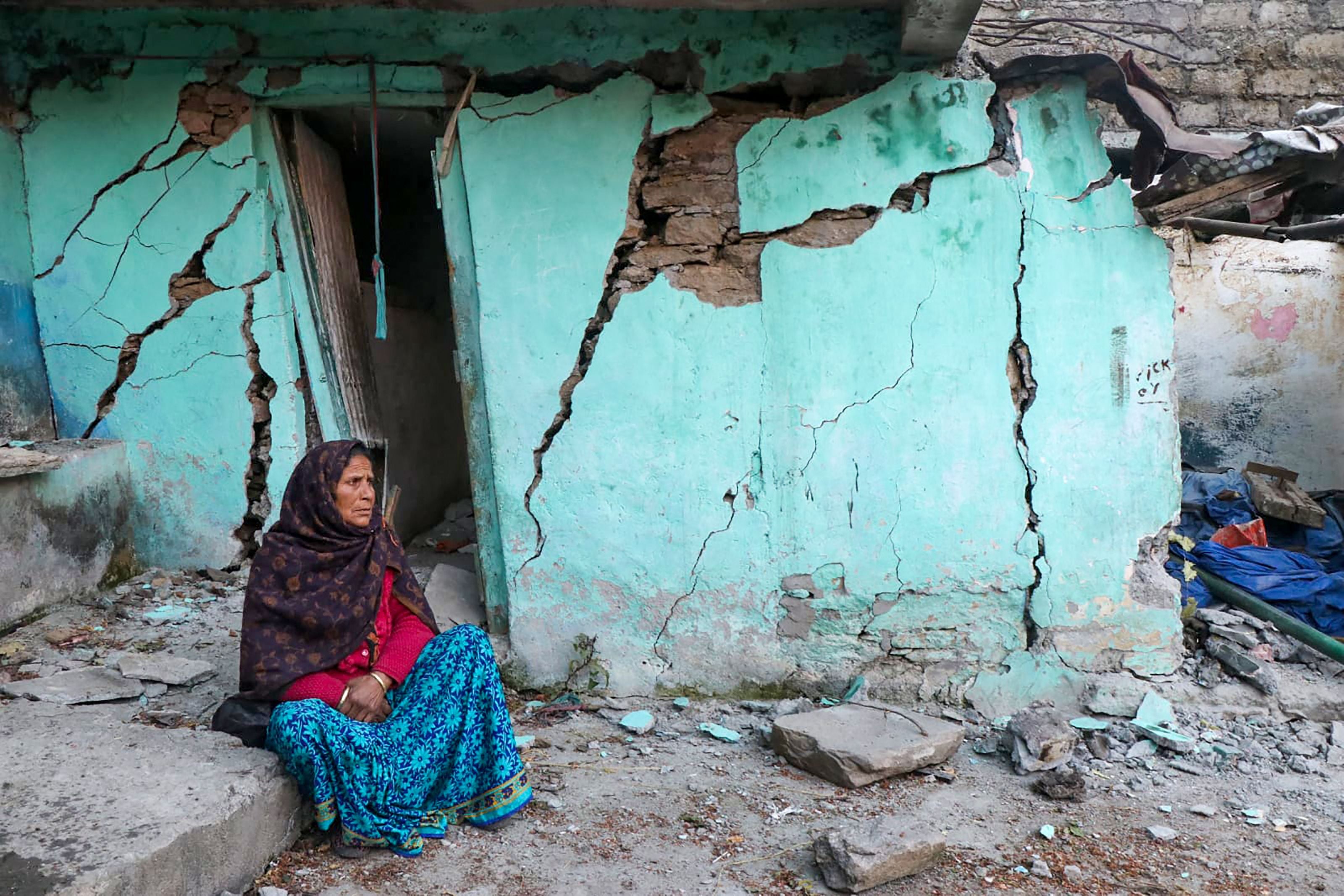 A woman sits beside a cracked wall of her house at Joshimath