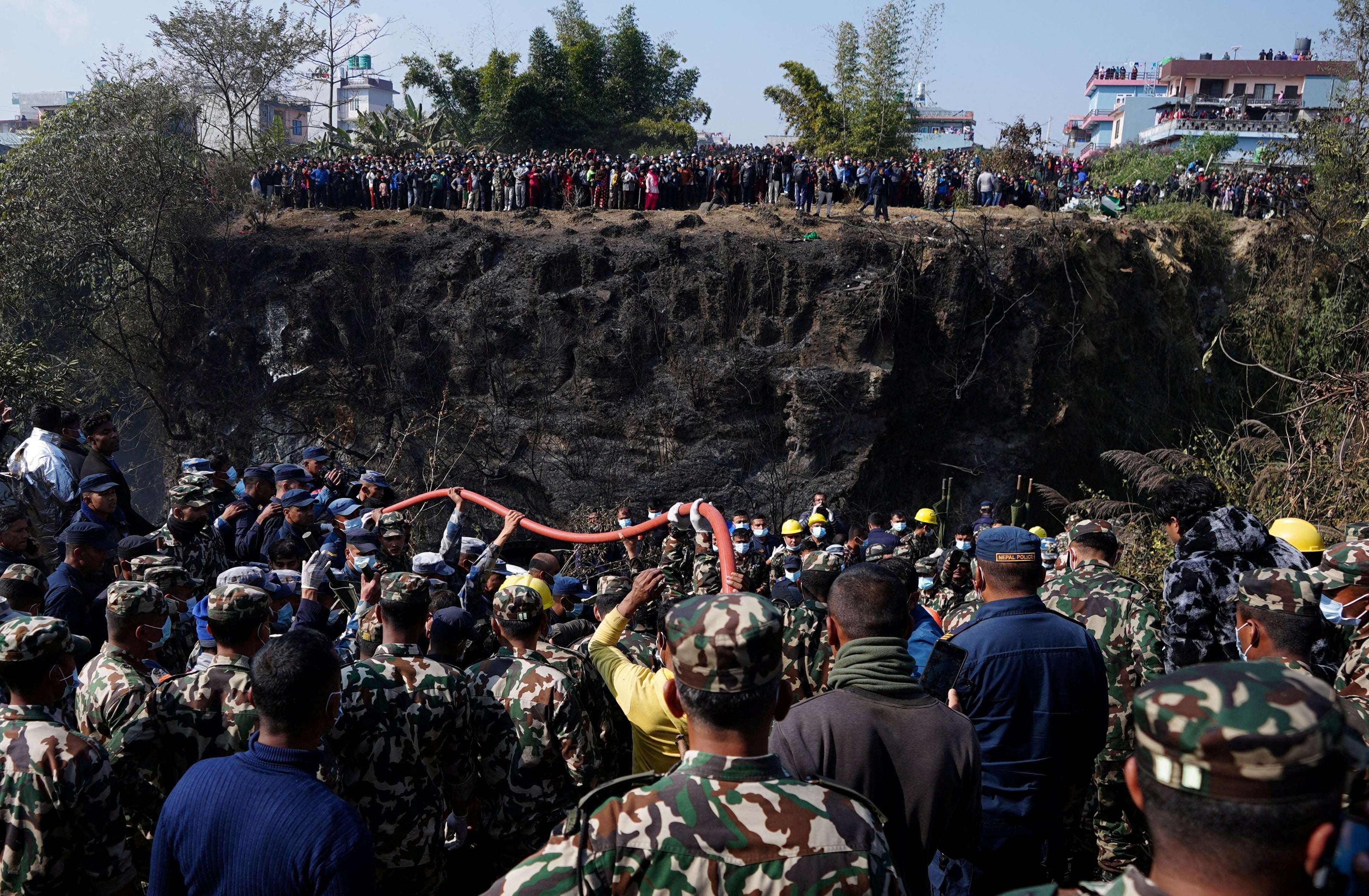 Crowds gather as rescue teams work to retrieve bodies at the crash site