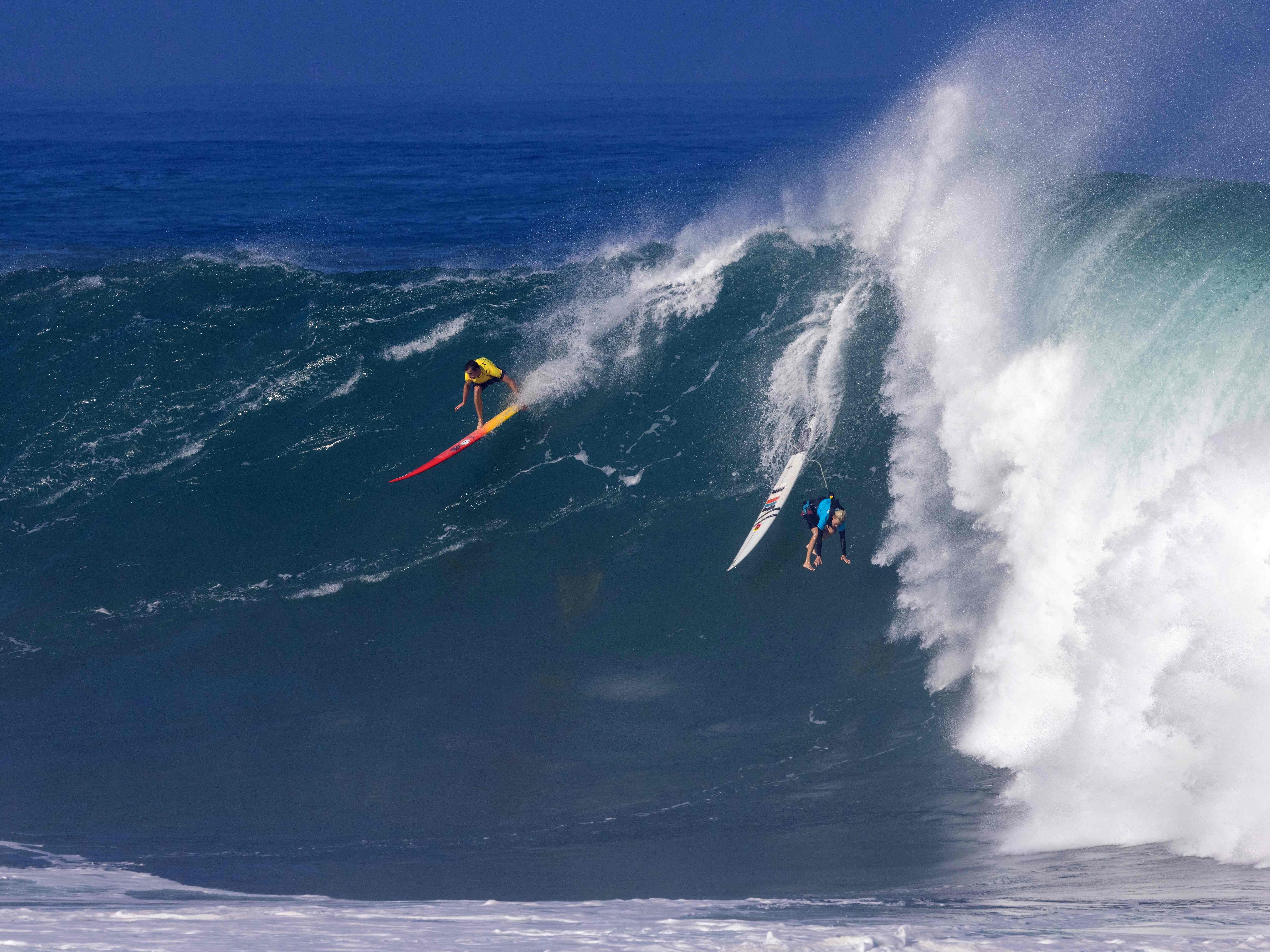 Hawaiian surfer Jake Maki rides a wave as Hawaiian surfer Keala Kennely gets wiped out during The Eddie Aikau Big Wave Invitational surfing contest on January 22, 2023