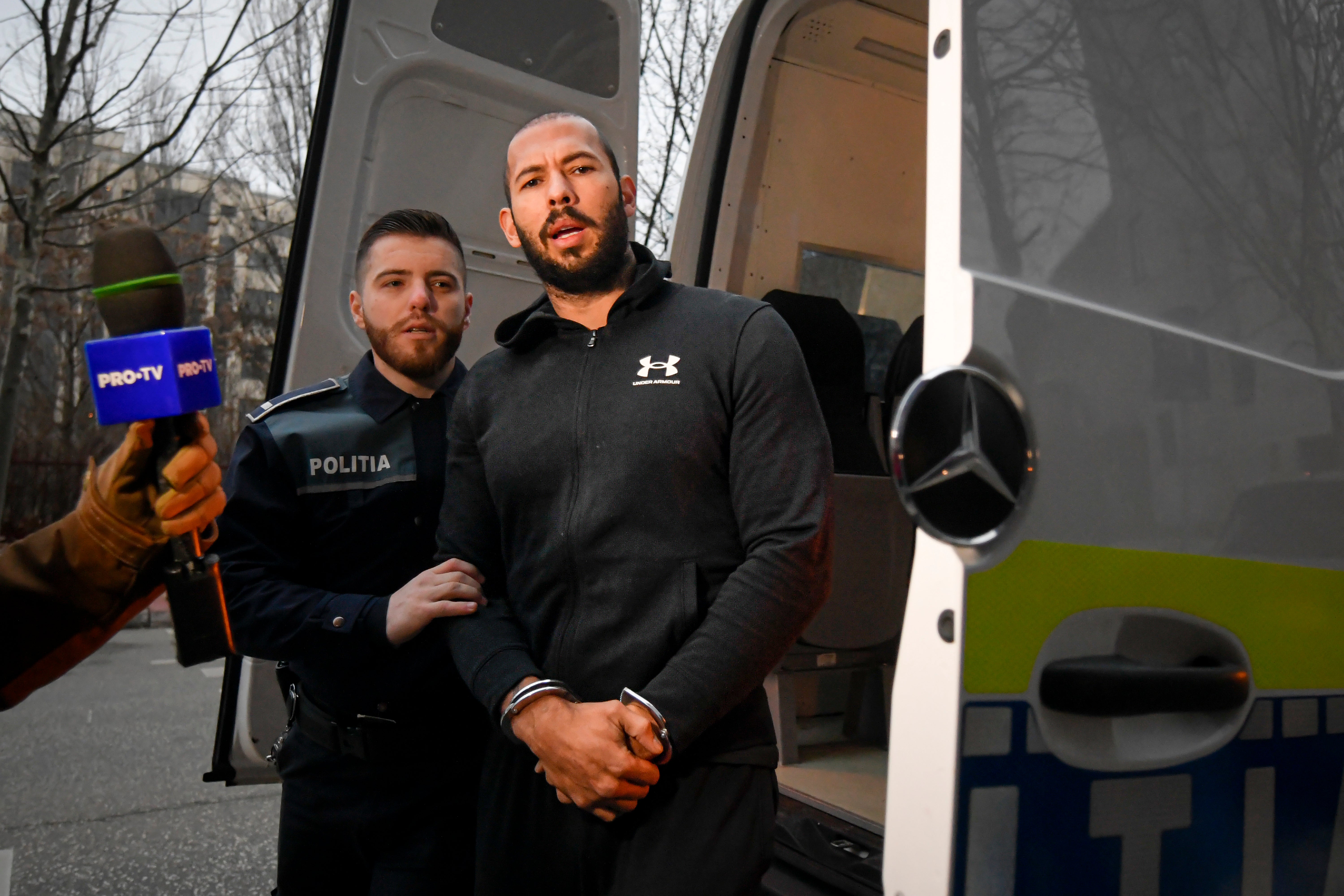 Police officers escort Andrew Tate outside the Directorate for Investigating Organized Crime and Terrorism (DIICOT) where prosecutors examine electronic equipment confiscated during the investigation in their case, in Bucharest, Romania