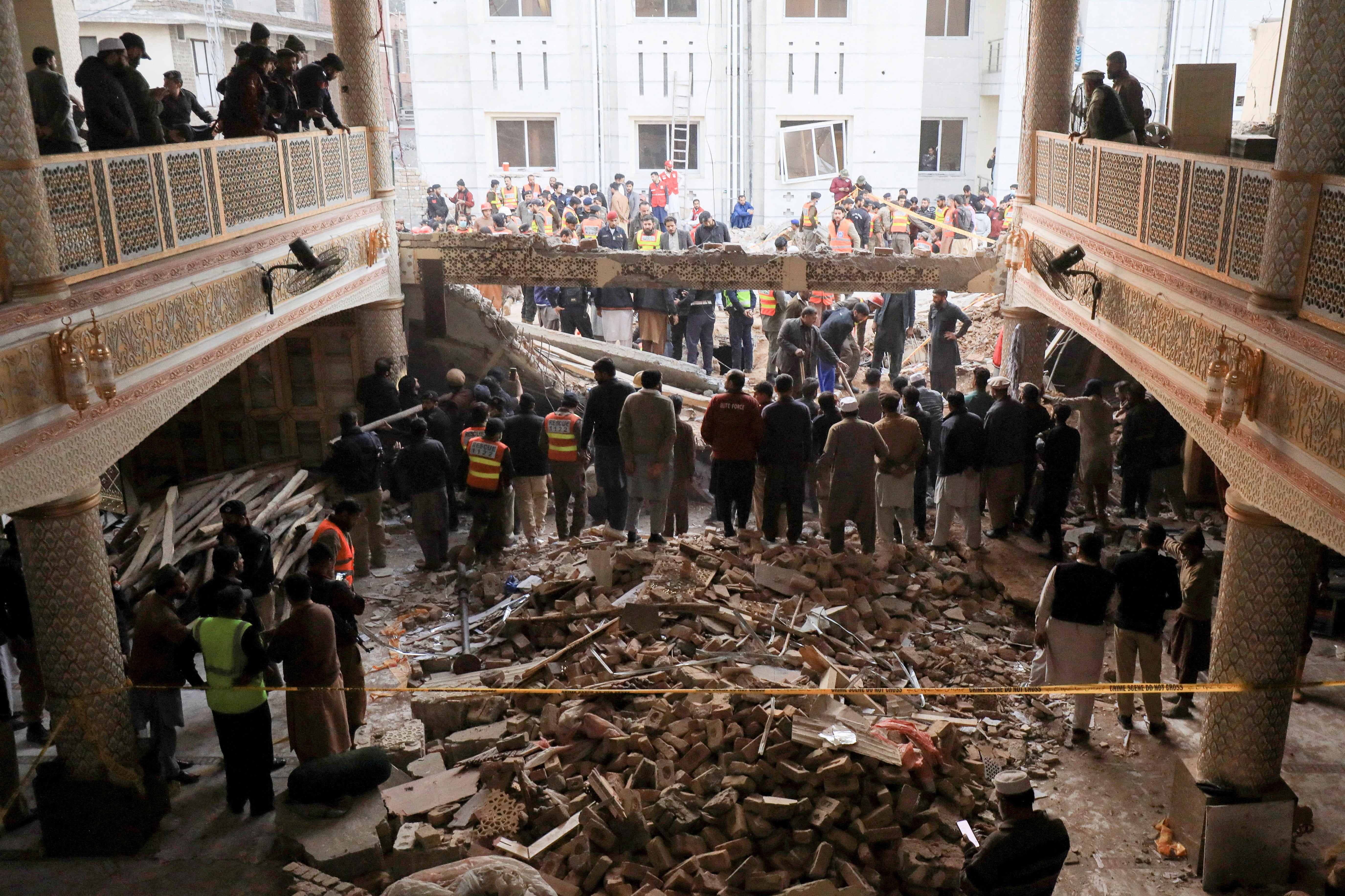 People and rescue workers gather to look for survivors under a collapsed roof, after a suicide blast in a mosque in Peshawar