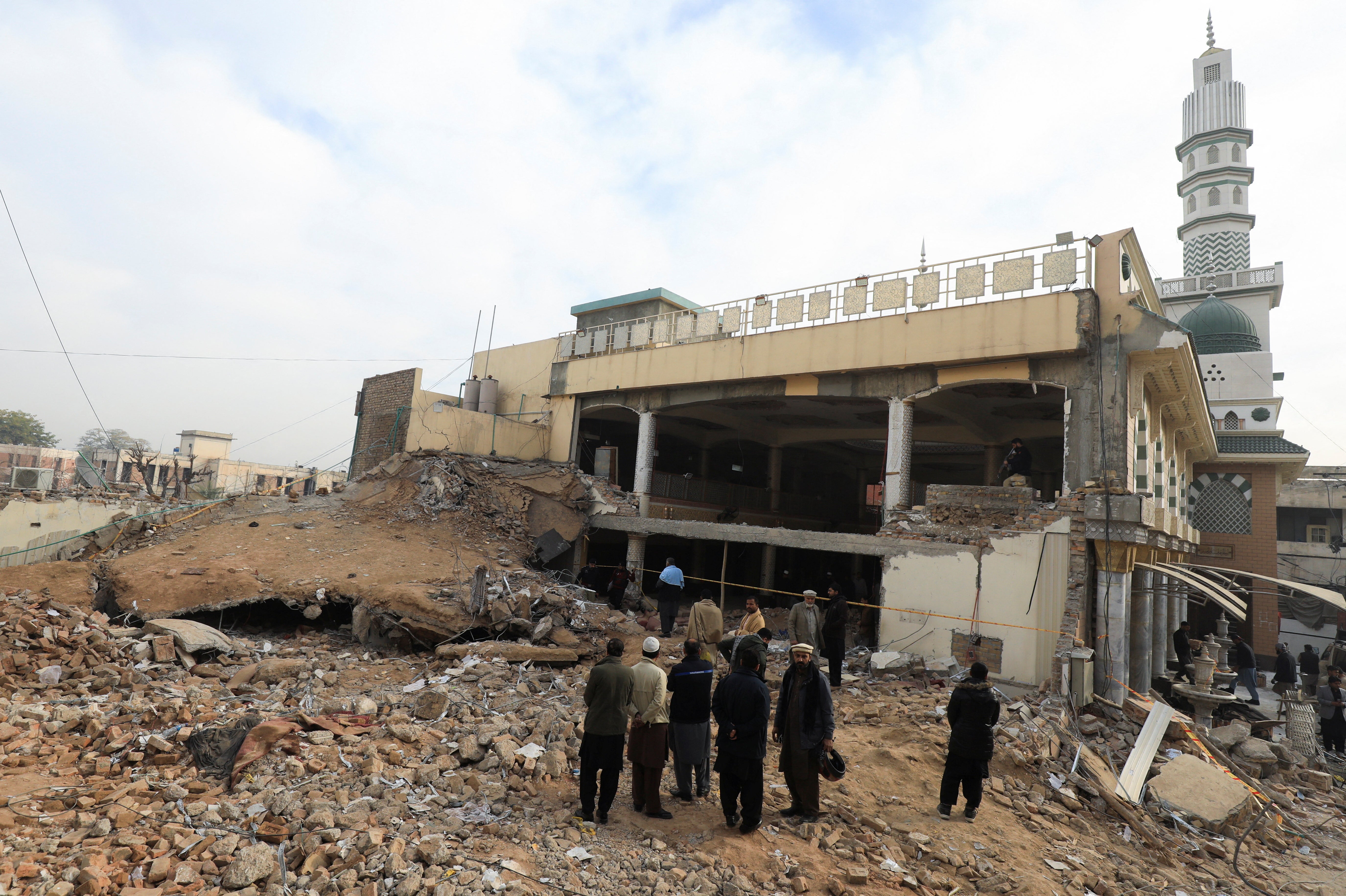 People stand amid the rubble, following a suicide blast in a mosque in Peshawar