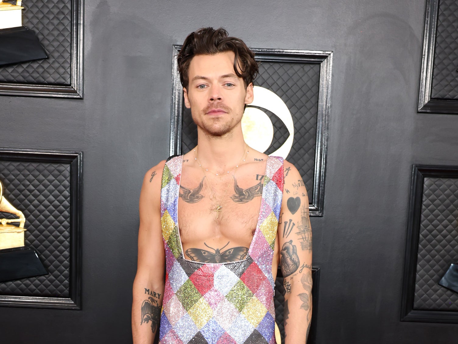 Harry Styles arrived on the red carpet in a multi-coloured sequin jumpsuit that revealed the bird tattoos on his chest