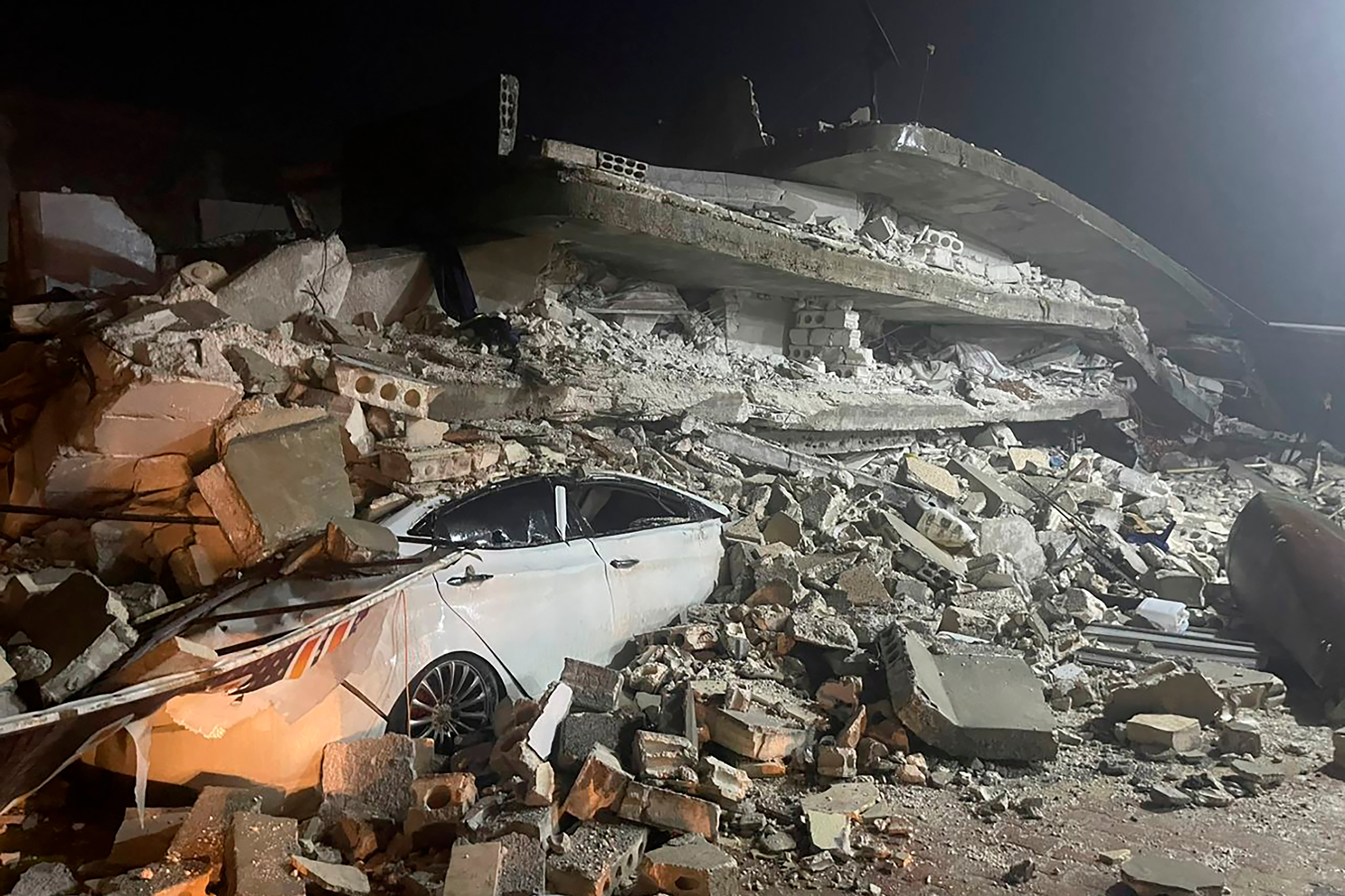 A car is seen under the wreckage of a collapsed building, in Azmarin town