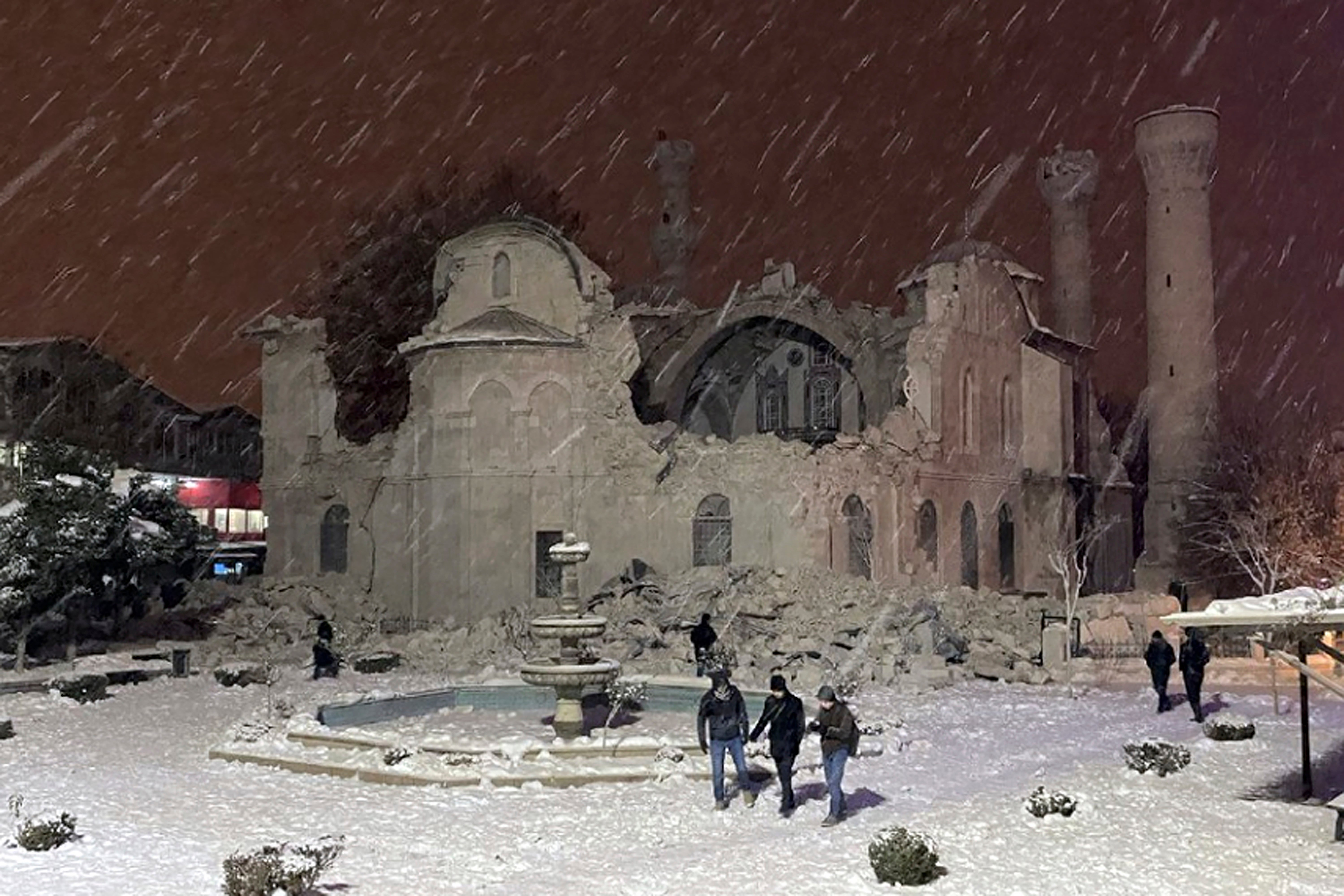 People walk next to a mosque destroyed by an earthquake in Malatya, Turkey