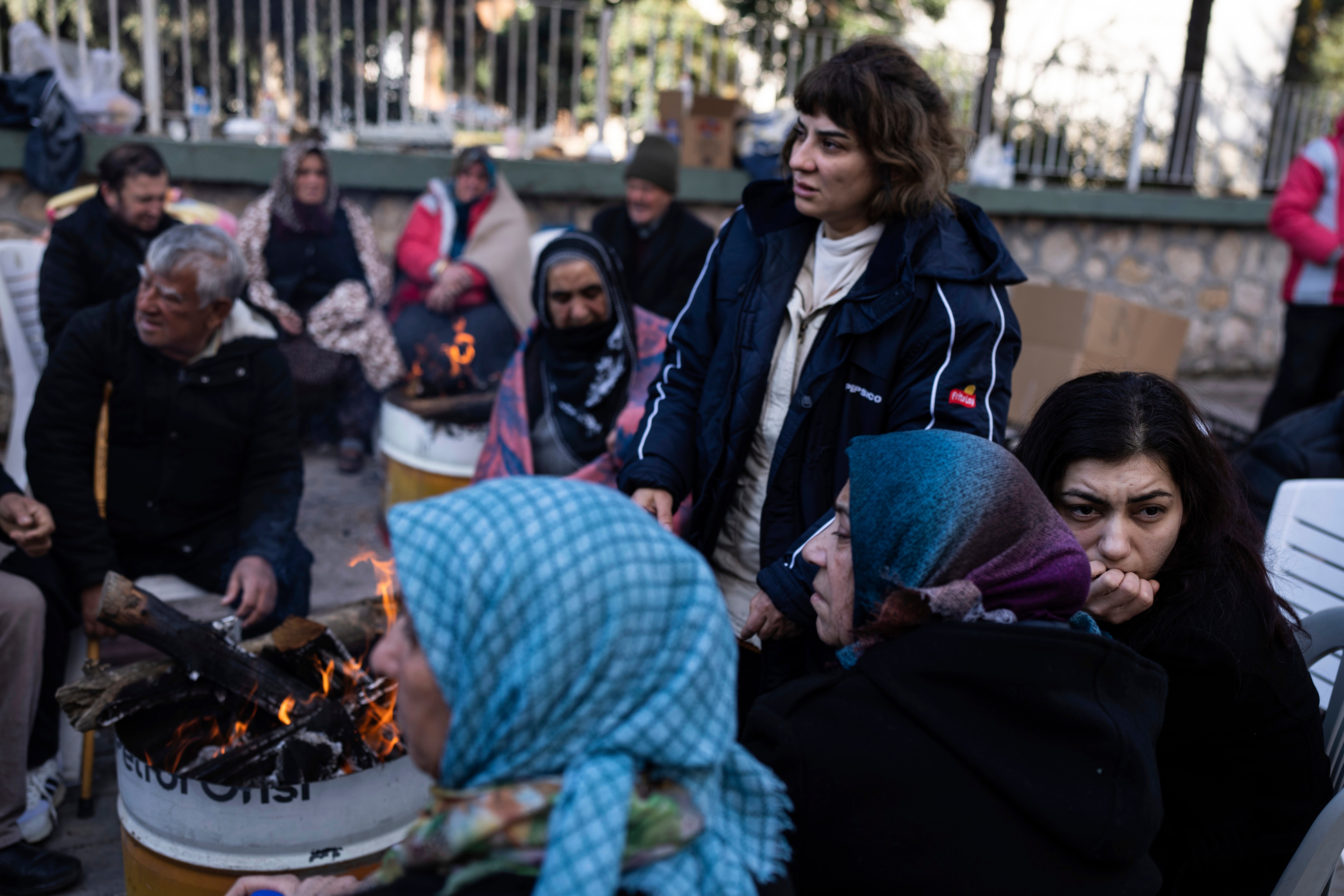 Locals sit around bonfire as firefighters and rescue teams search for people in a destroyed building, in Adana, southern Turkey