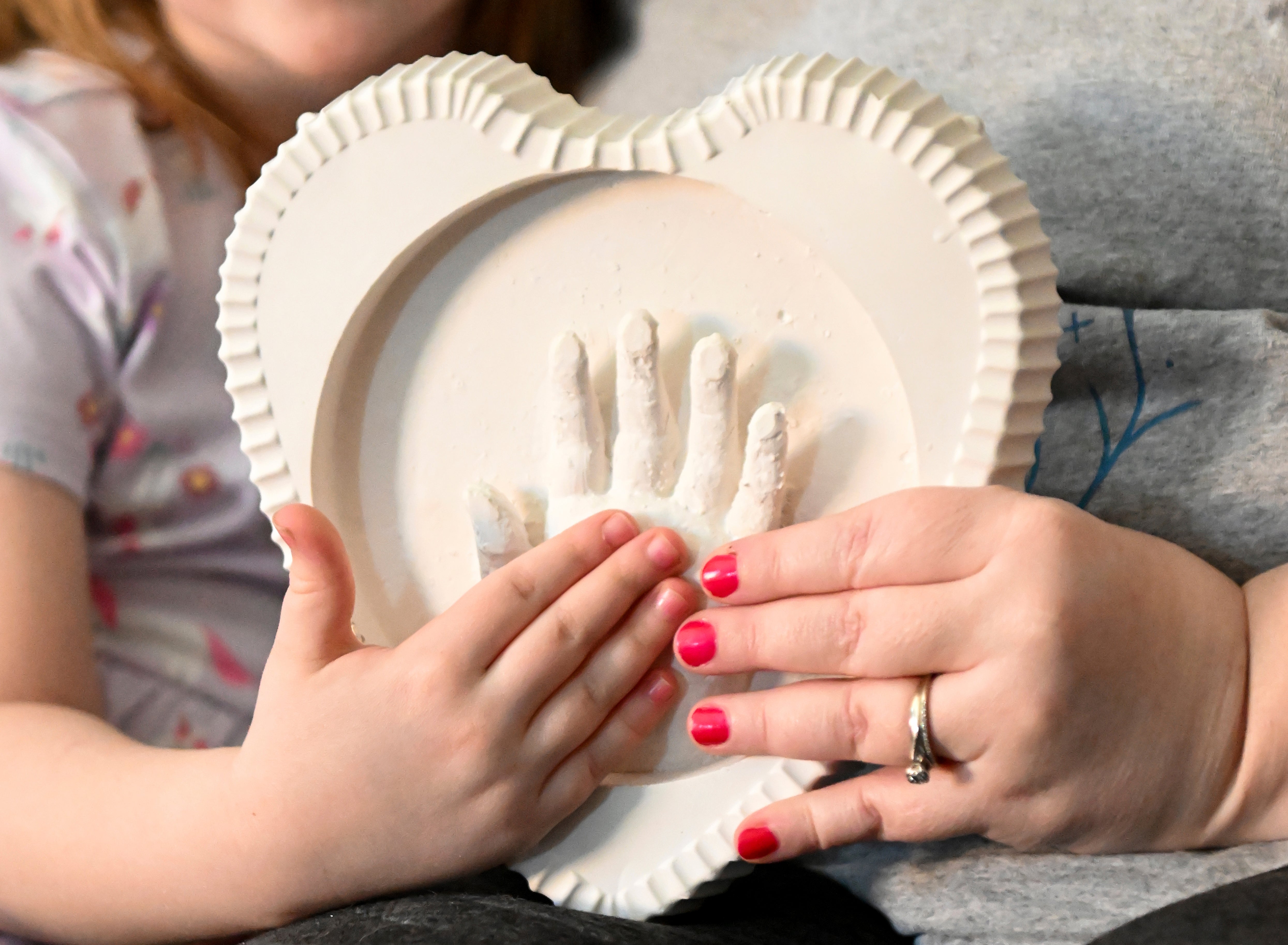 Jessica Day-Weaver right, and Caitlin Weaver hold up a ceramic hand print of daughter, Anastasia, at their home, Thursday, Feb. 2, 2022, in Boardman, Ohio