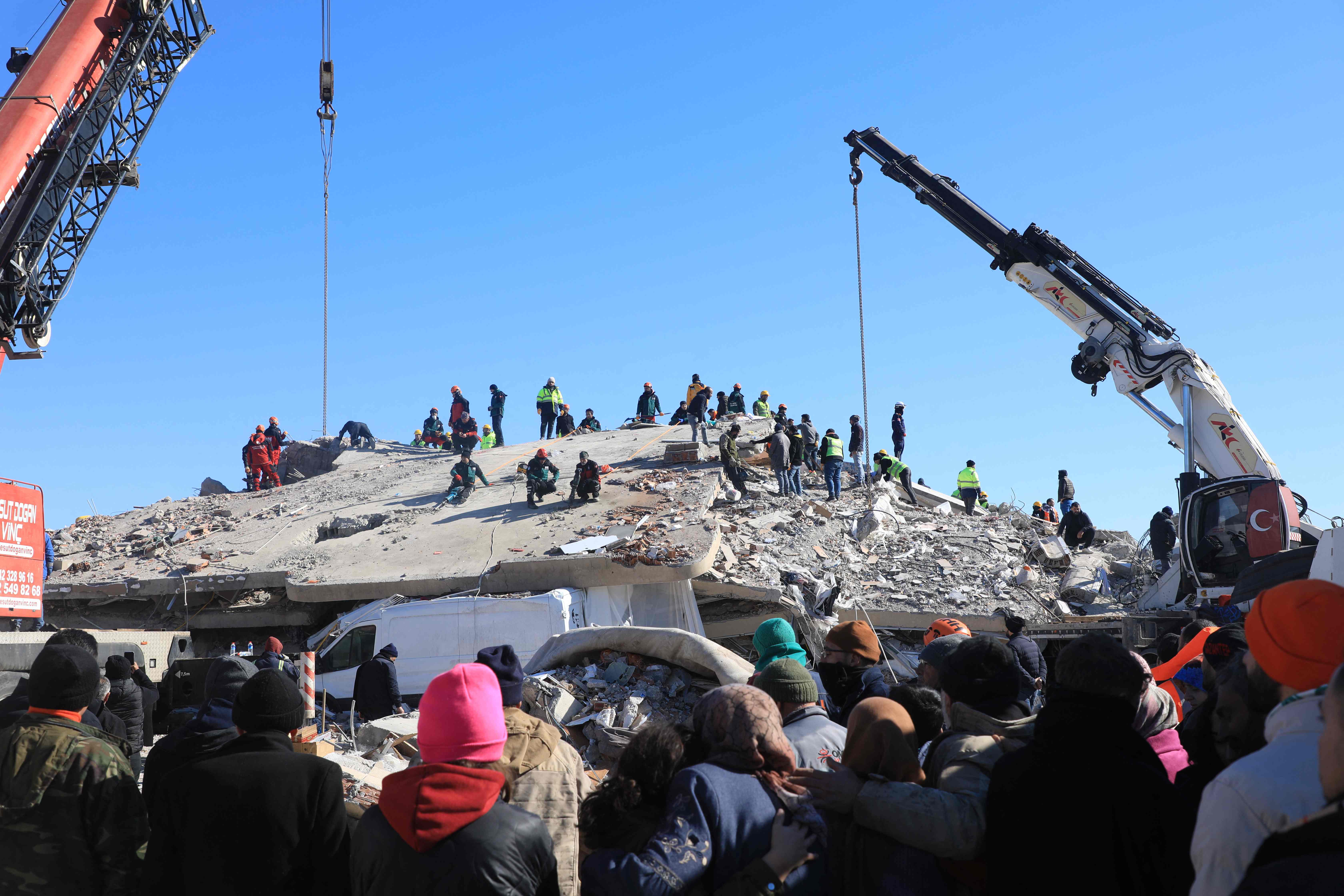 People watch as rescuers and civilians look for survivors under the rubble of collapsed buildings in Nurdagi