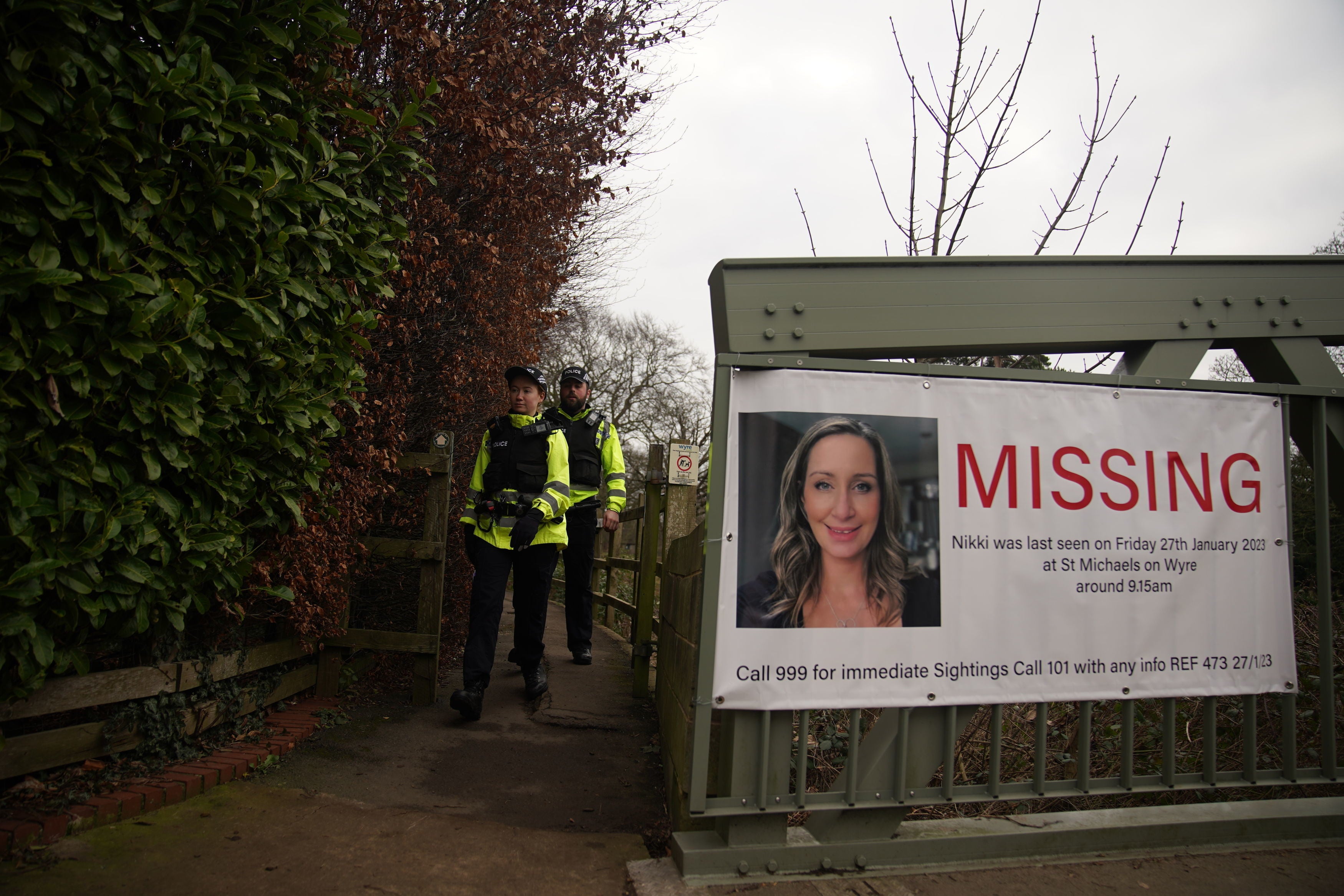 Police officers walk towards a missing person appeal poster for Nicola Bulley on a bridge over the River Wyre