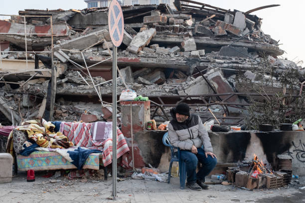 A man sits near a collapsed building as she waits news from her loved ones on 13 February 2023 in Hatay, Turkey