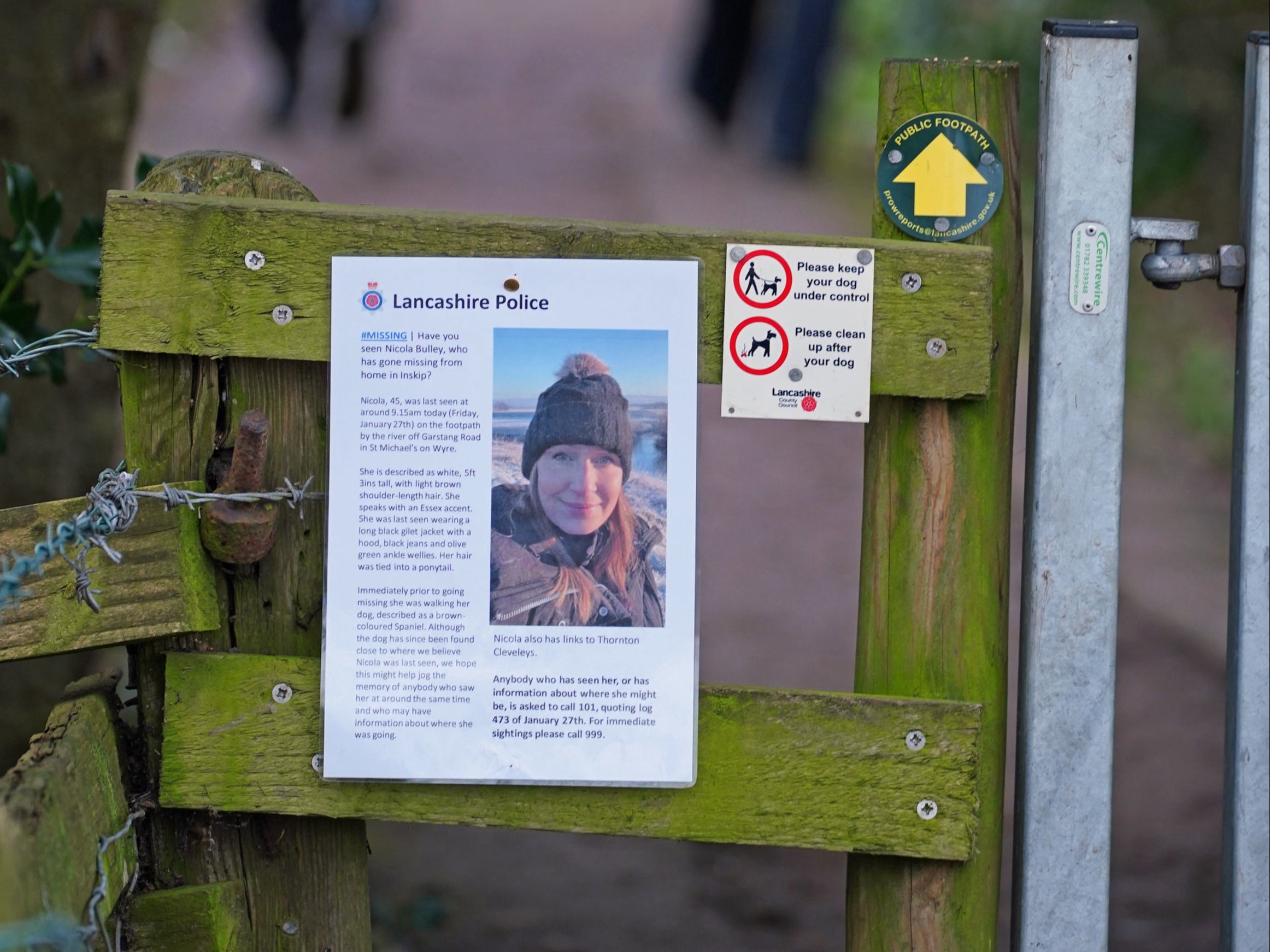 A missing person appeal poster for Nicola Bulley as police officers walk along a footpath in St Michael's on Wyre