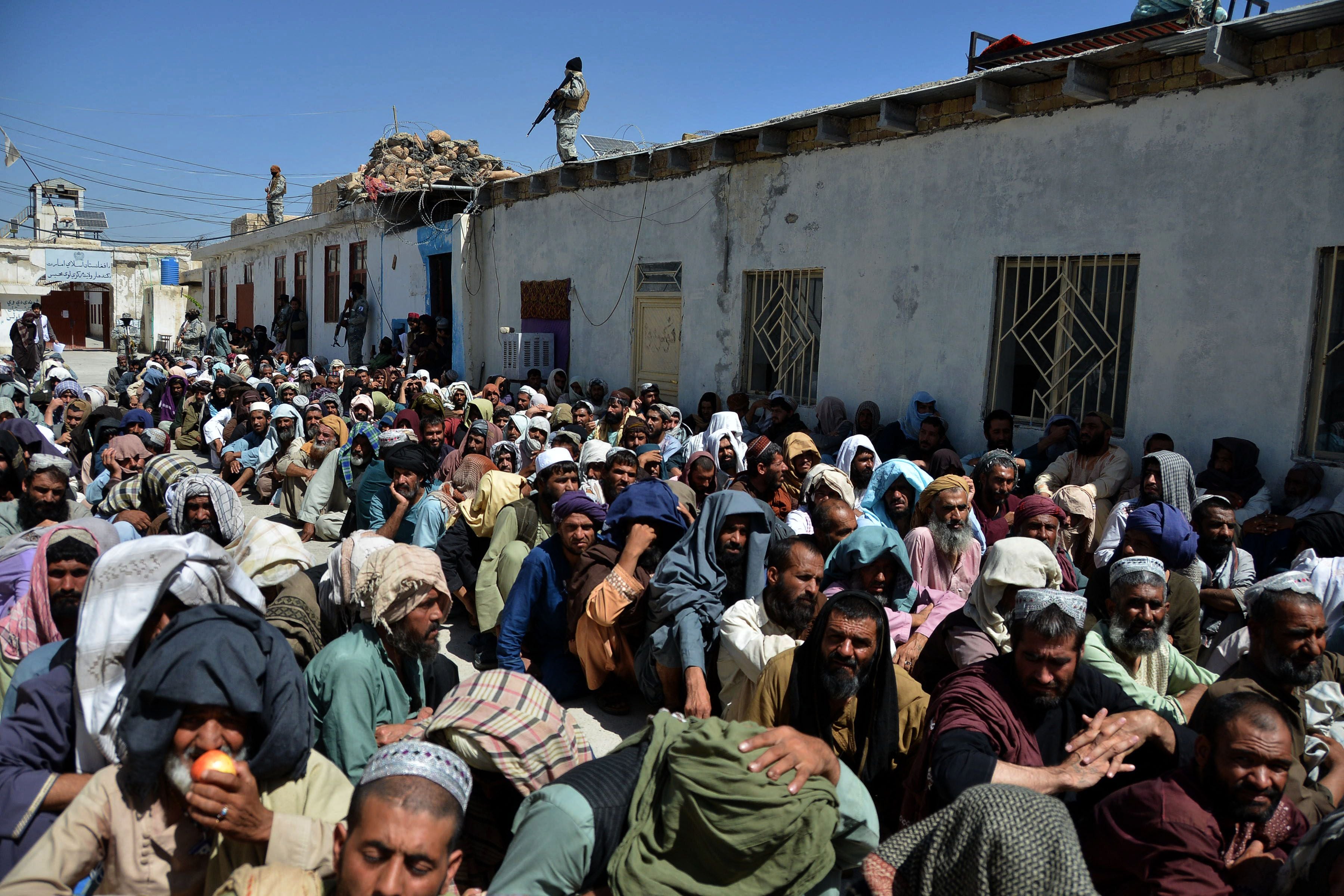 A Taliban soldier stands guard on a roof as men imprisoned for drug use sit in a courtyard before their release from Kandahar Central Prison