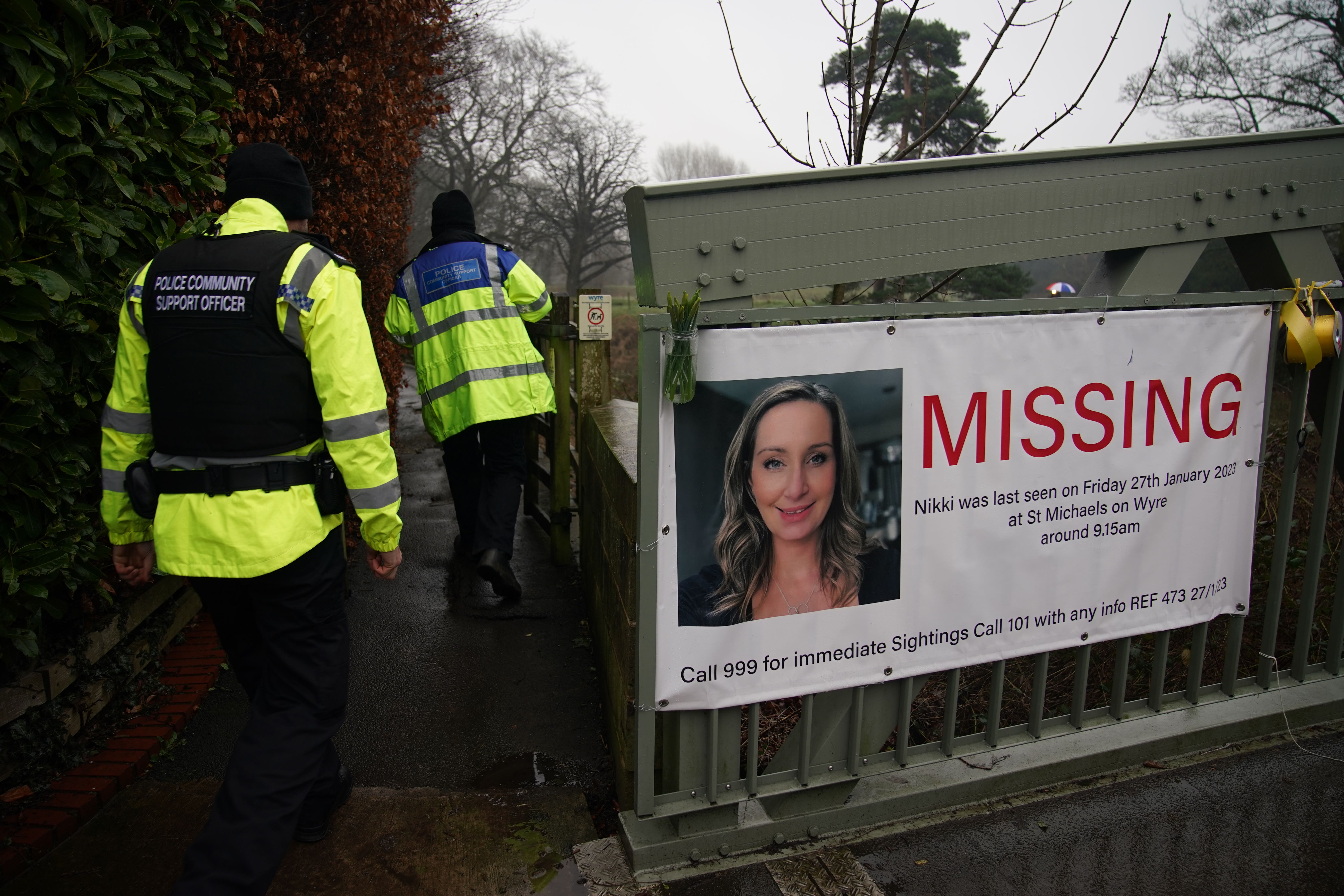 Police officers walk past a missing person appeal poster for Nicola Bulley tied to a bridge in St Michael’s on Wyre