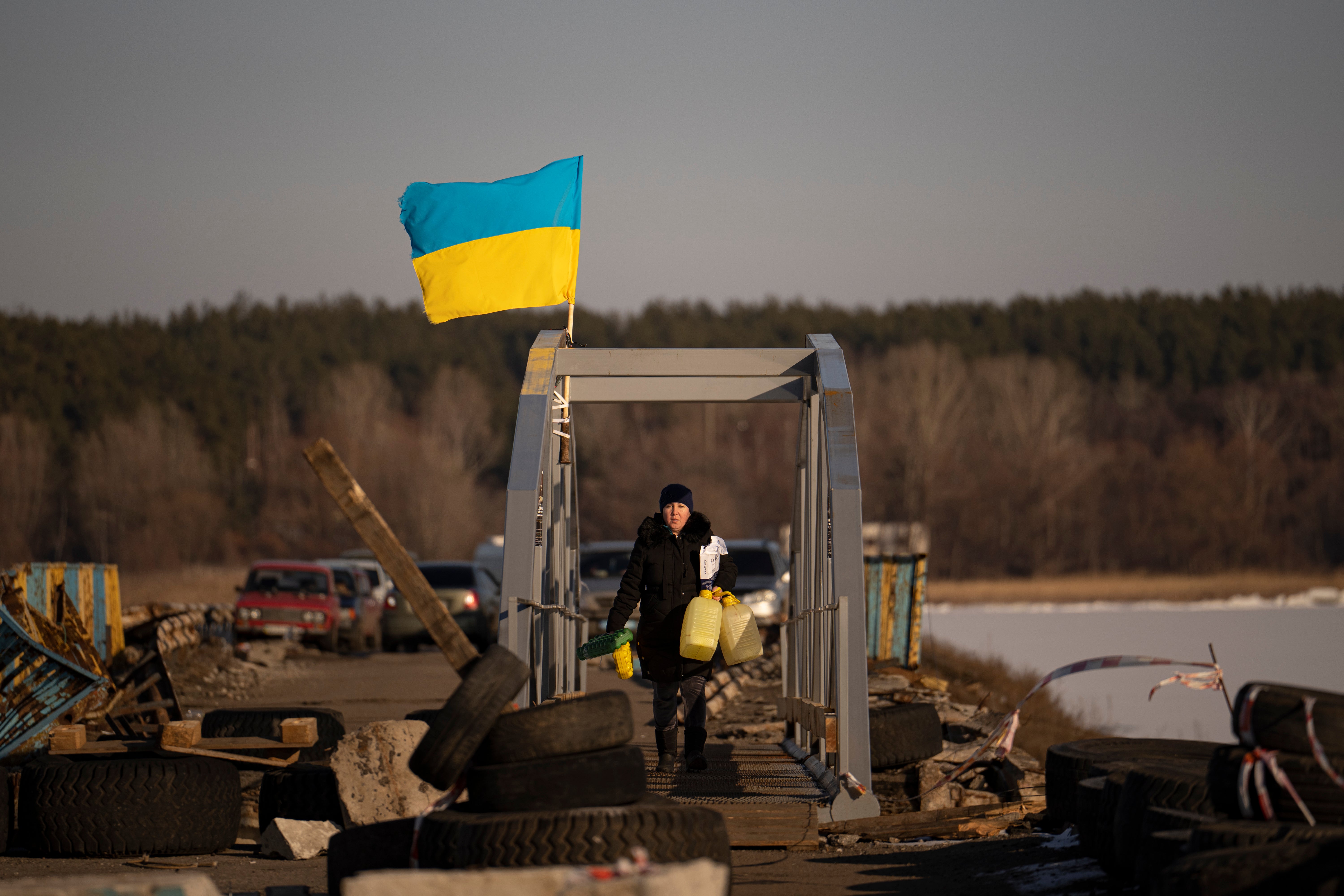 A woman crosses a makeshift pedestrian bridge connecting the two sides of a destroyed road bridge in Staryi Saltiv, Ukraine