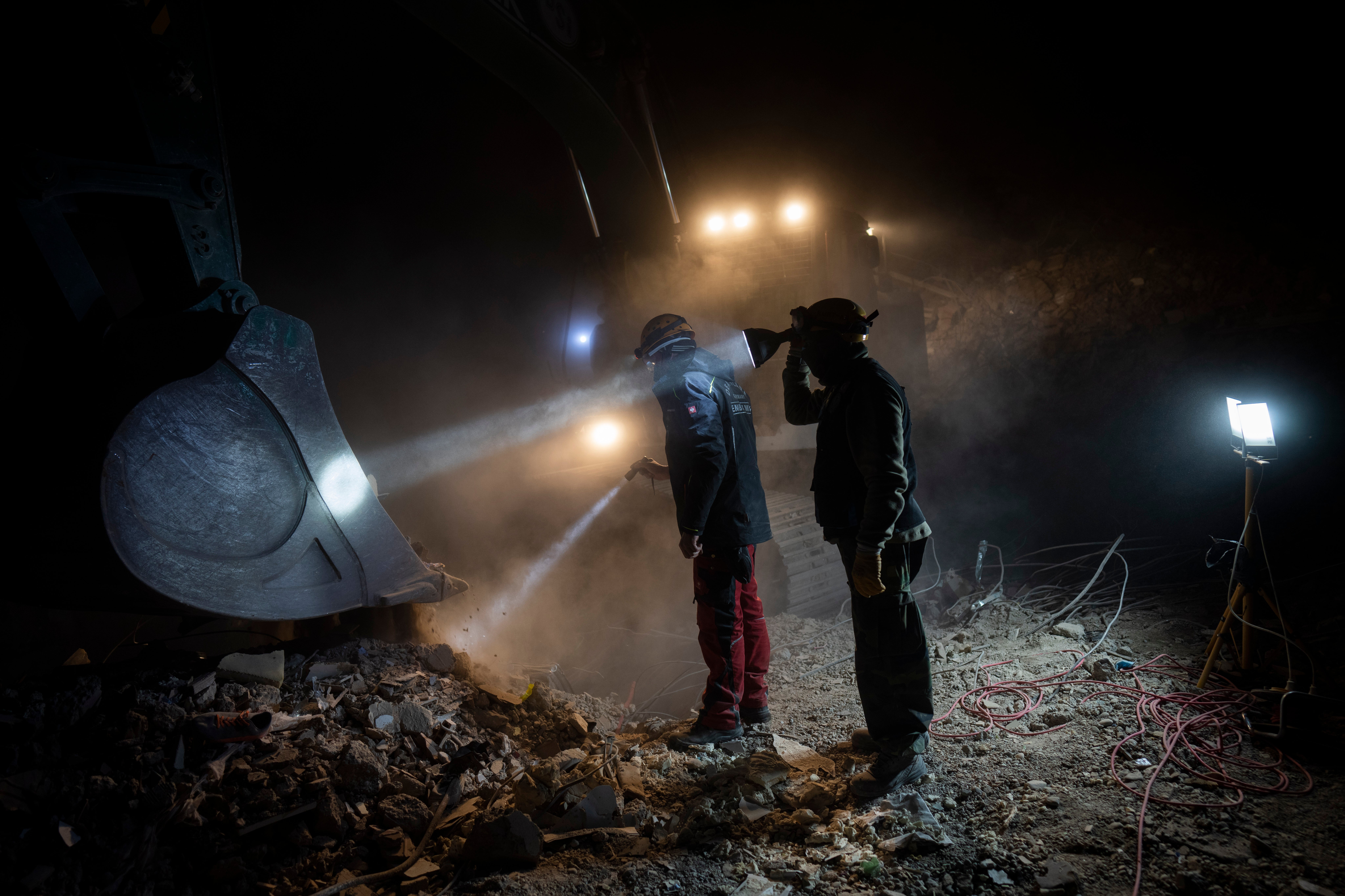 Members of NGOs Deathcare Embalming Team, left, and Turkish Kurt-Ar inspect the bucket of an excavator as they search for bodies of people who died during the earthquake in Kahramanmaras