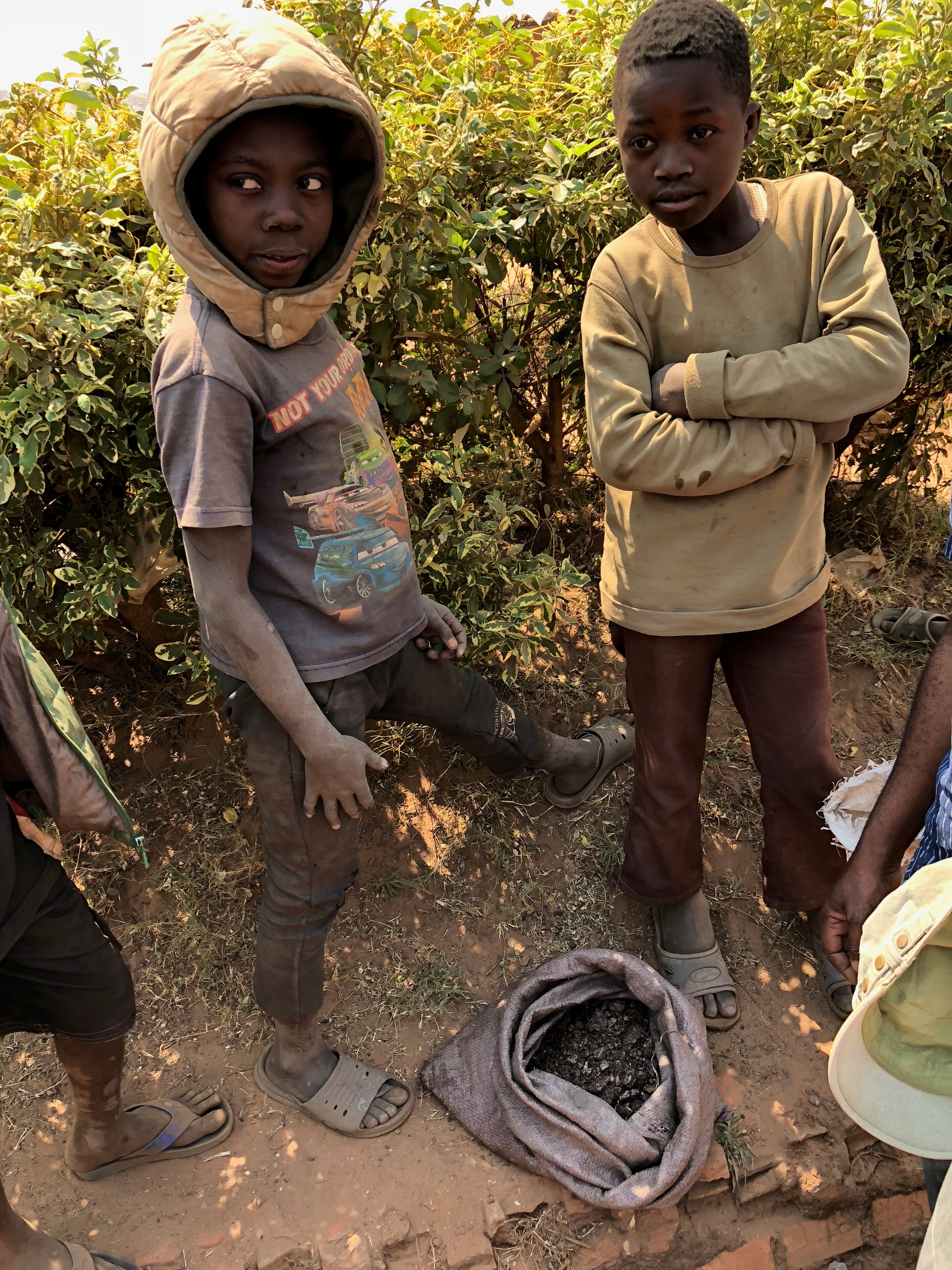 Two boys stand over their sack of scraps of cobalt. Thousands of children are mining for cobalt in the DRC as their families cannot afford to pay school fees on meagre wages