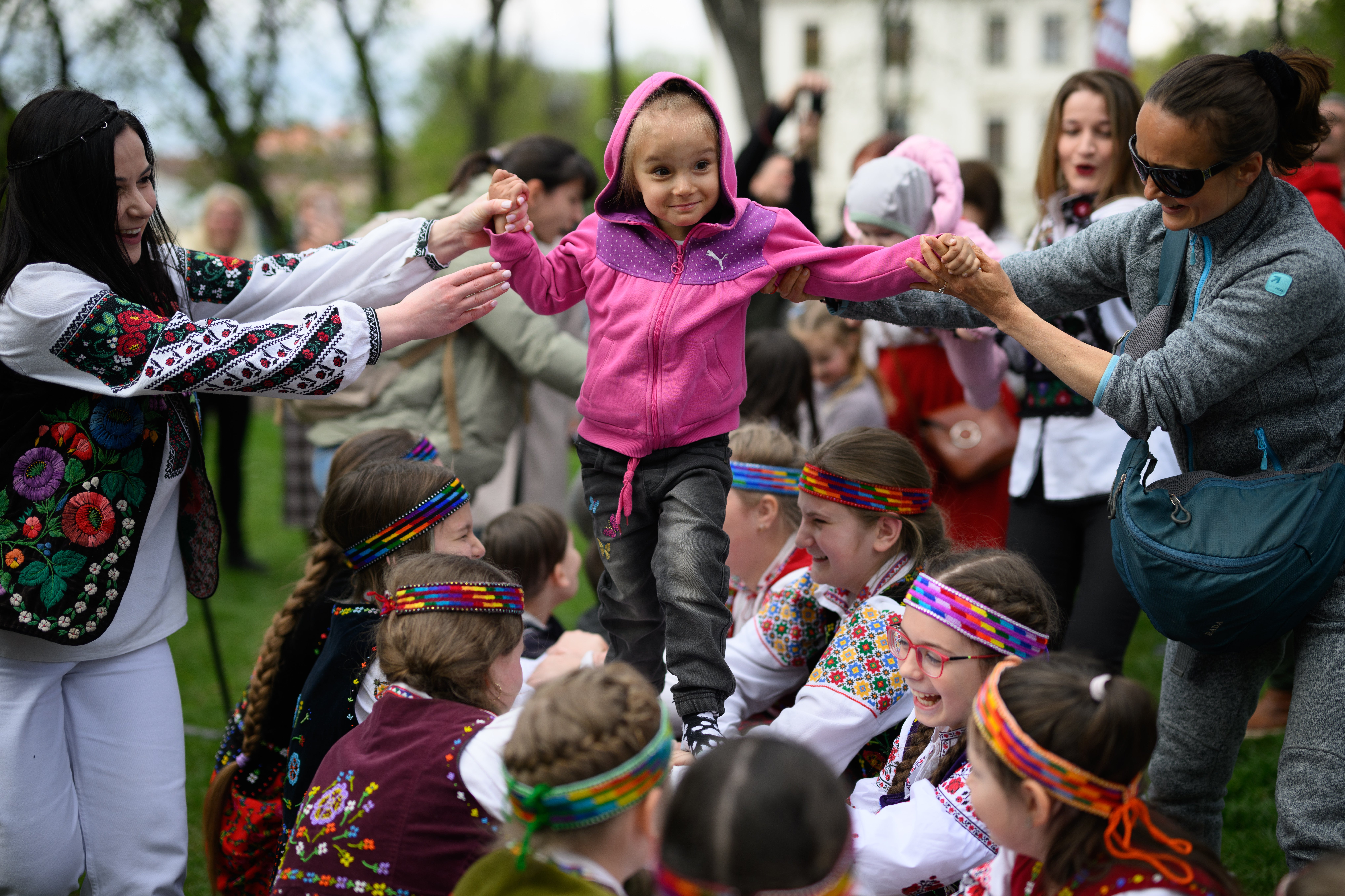 A young refugee child from Eastern Ukraine grins as she walks on the arms of a group of traditionally-dressed local children as they play Ukrainian children's games