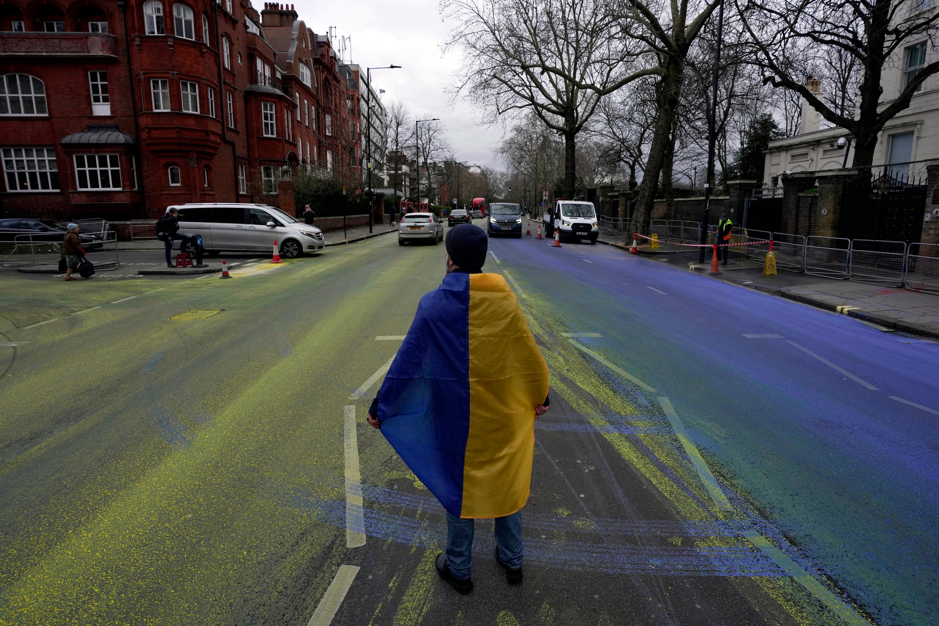 A protester wears a Ukraine flag after a group of activist artists painted a giant Ukrainian flag outside the Russian Embassy