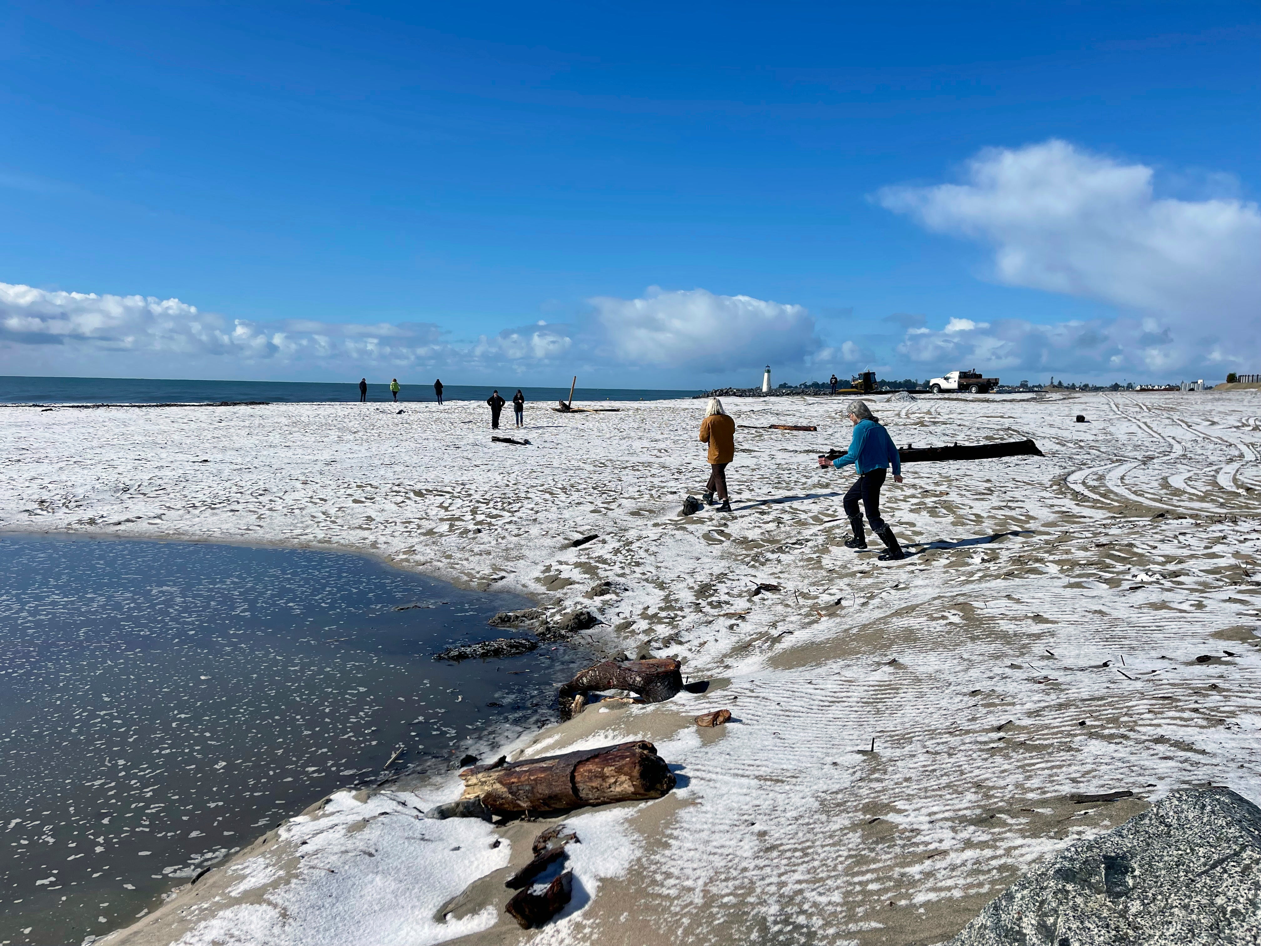 People walk along a snow covered Twin Lakes State Beach in Santa Cruz, Calif., on Thursday (Karen Krenis via AP)