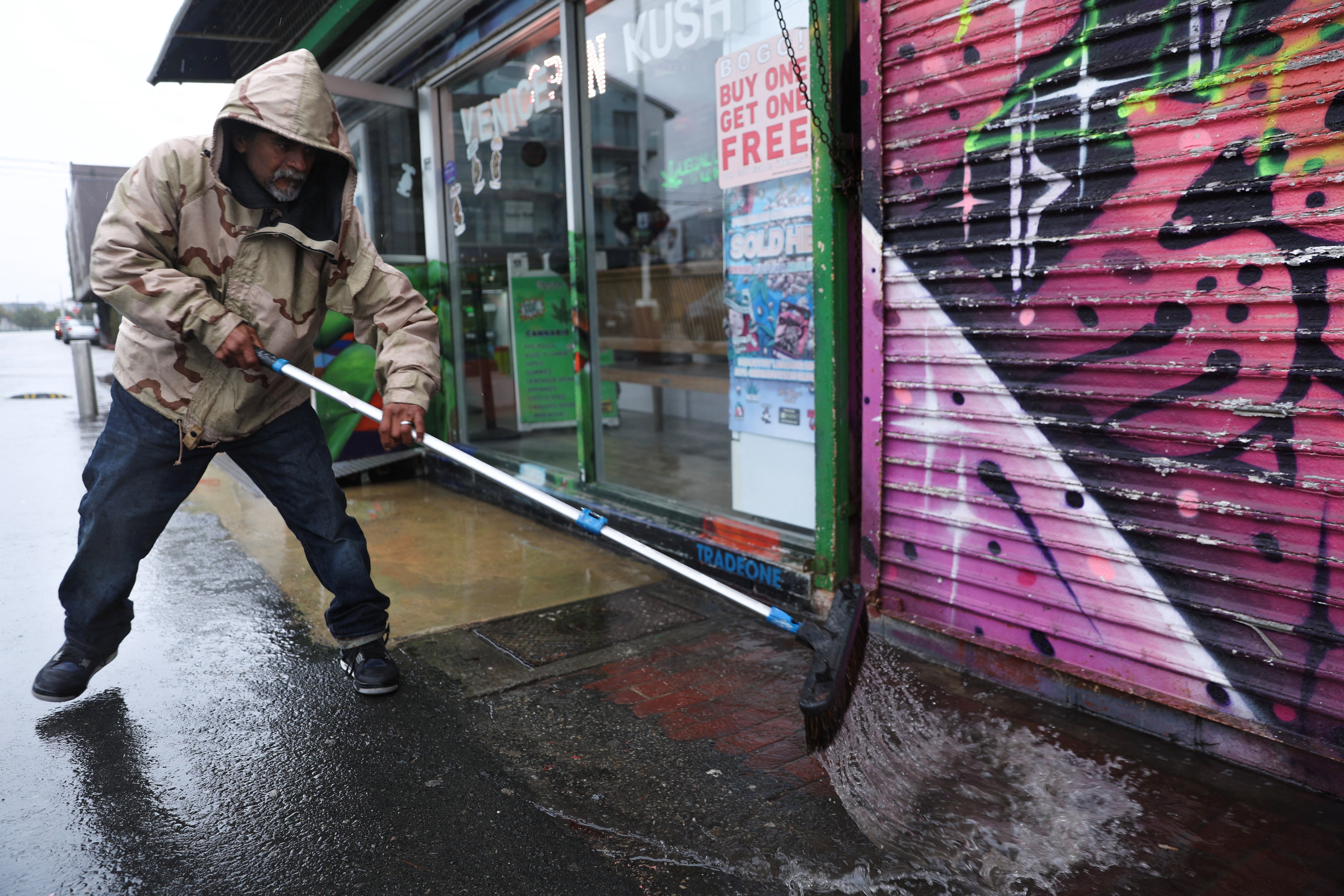 A worker uses a broom to sweep rain water from a shop along the Venice Beach Boardwalk