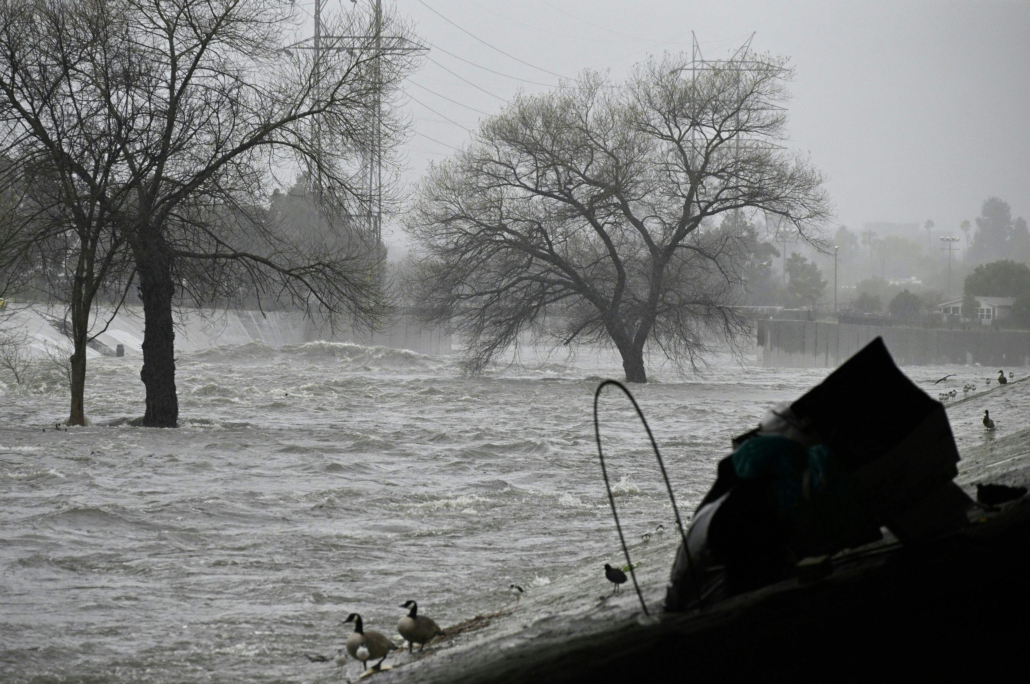 A homeless person’s tent is seen under a roadway overpass as water rushes down the Los Angeles River channel near Griffith Park