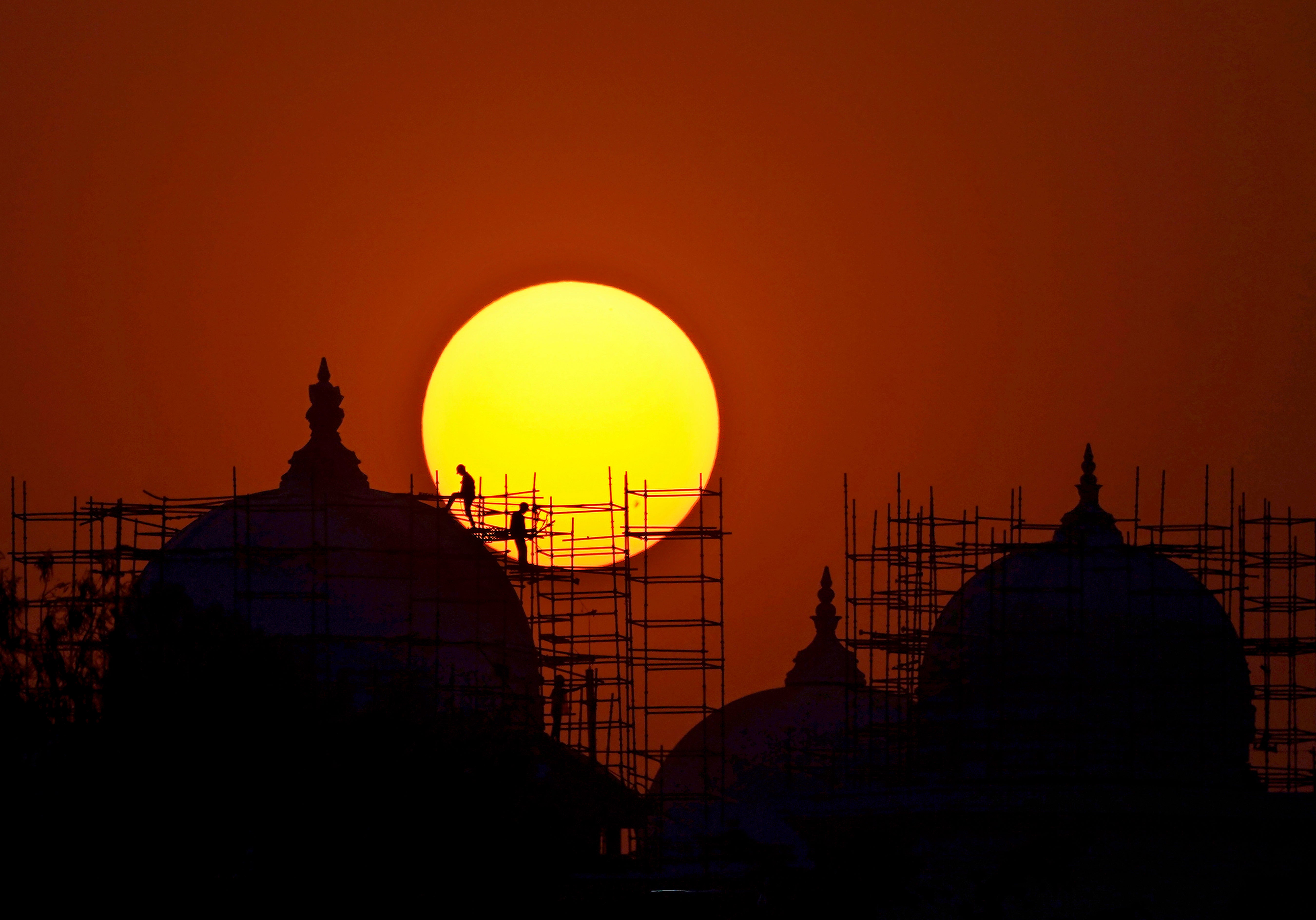 Workers are silhouetted against the setting sun at a construction site of a new Telangana State Secretariat building in Hyderabad, India