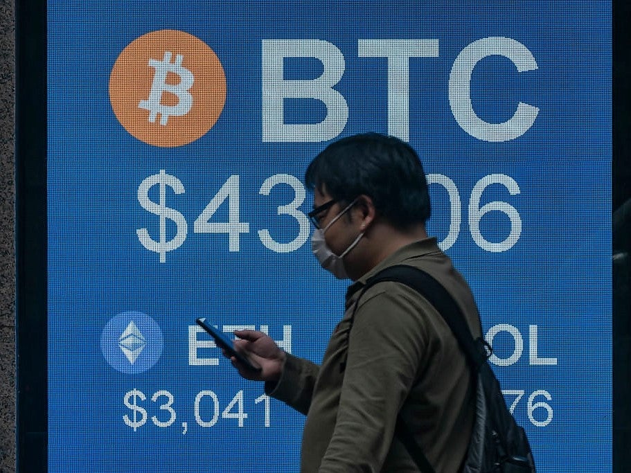 A pedestrian walks past a digital screen displaying the prices of cryptocurrencies bitcoin on 15 February, 2022, in Hong Kong