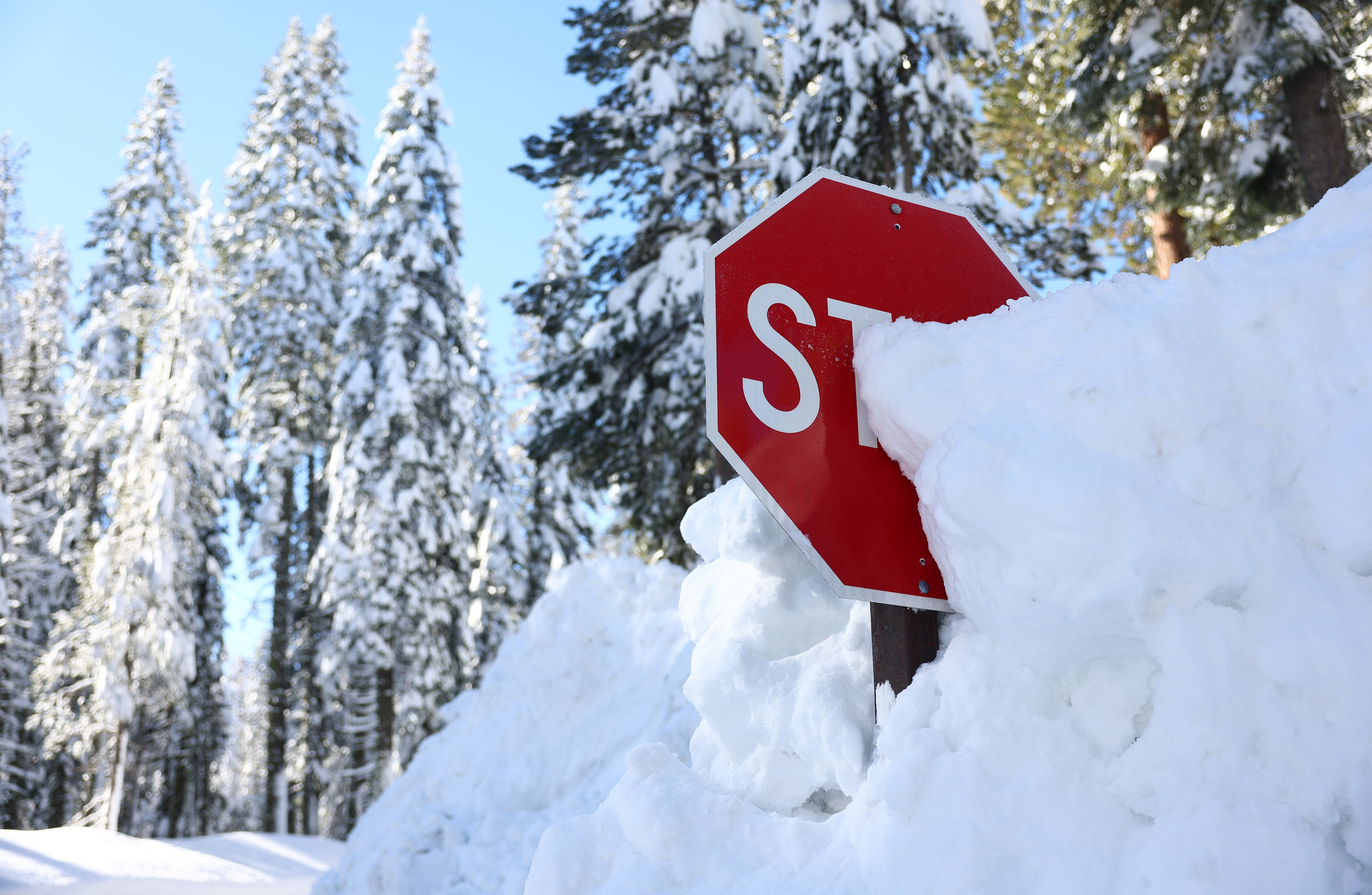 A stop sign is partially buried in a snowbank after a series of atmospheric river storms on January 20, 2023 in Yosemite National Park, California